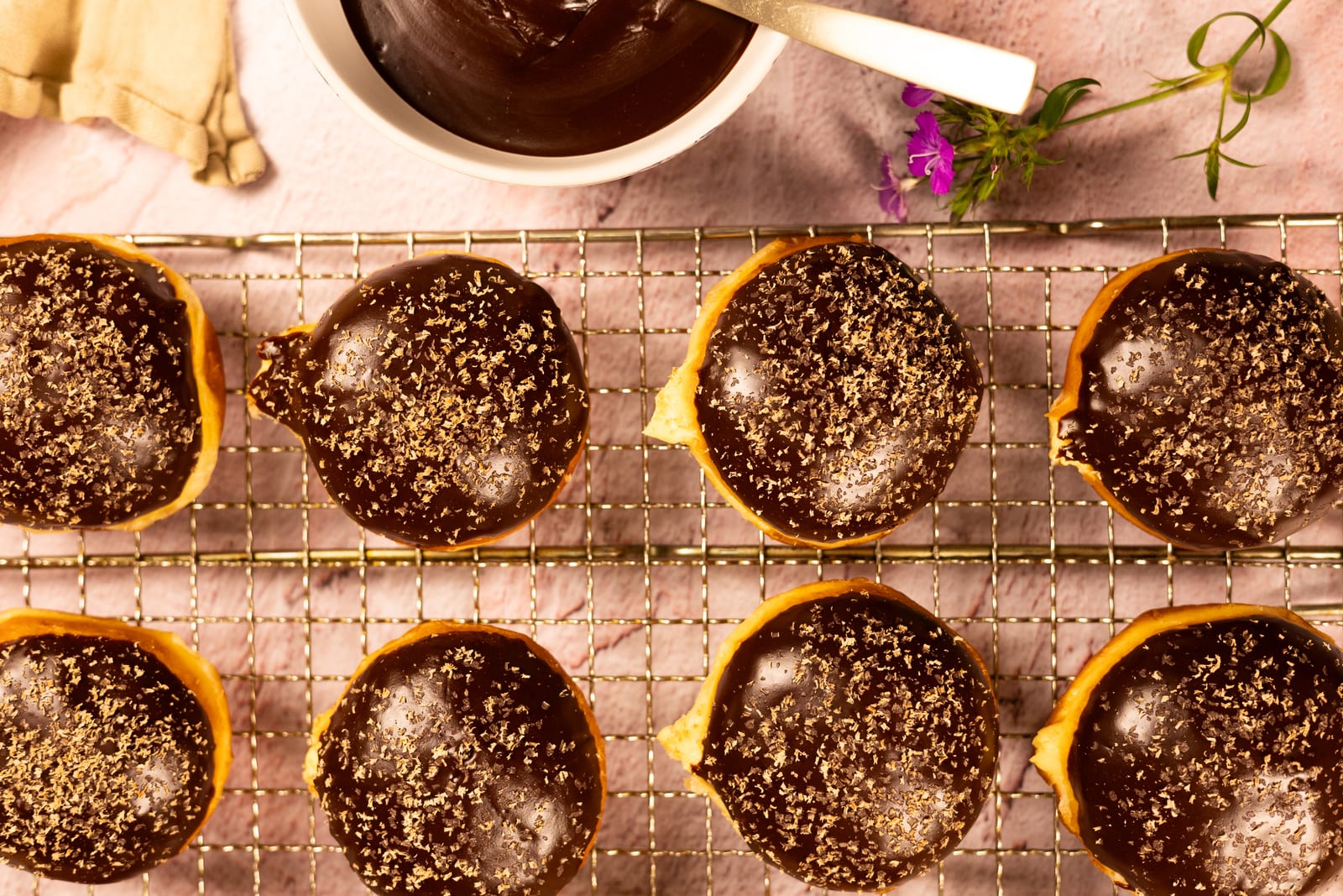 Chocolate-glazed brioche donuts in rows on a wire rack, from above
