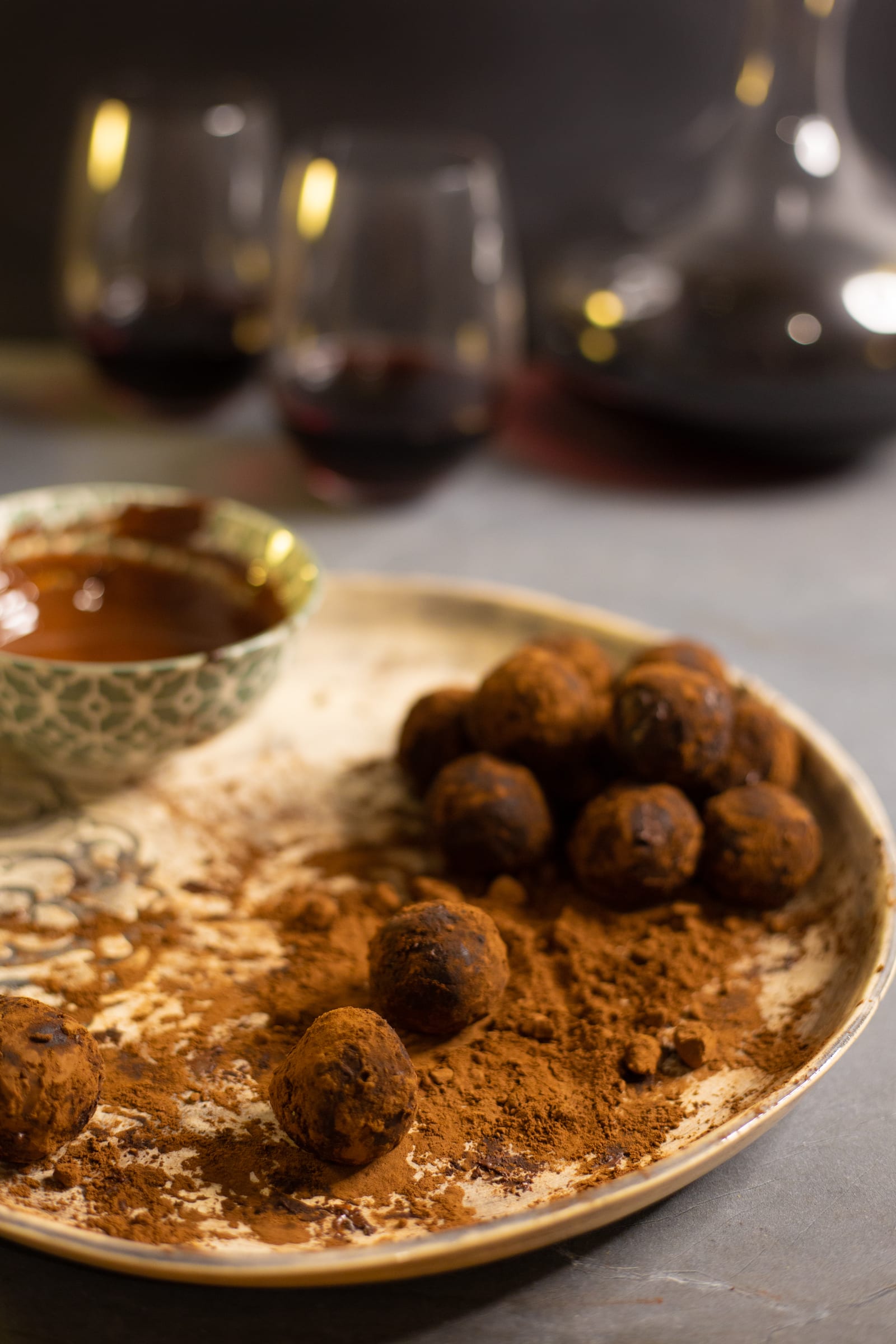 A pile of rum and raisin truffles on a patterned plate, wine glasses behind