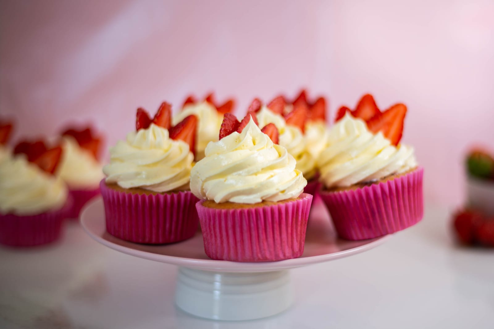 Strawberry and white chocolate cupcakes on a white cake stand against a pink wall