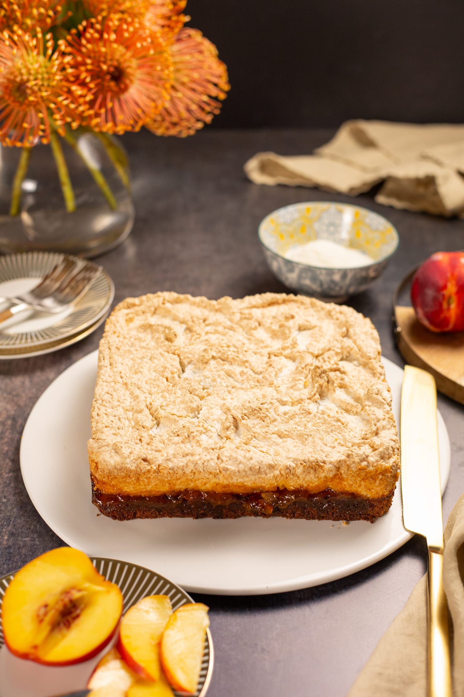 The whole hertzoggie slice on a plate before cutting, with peaches and orange flowers