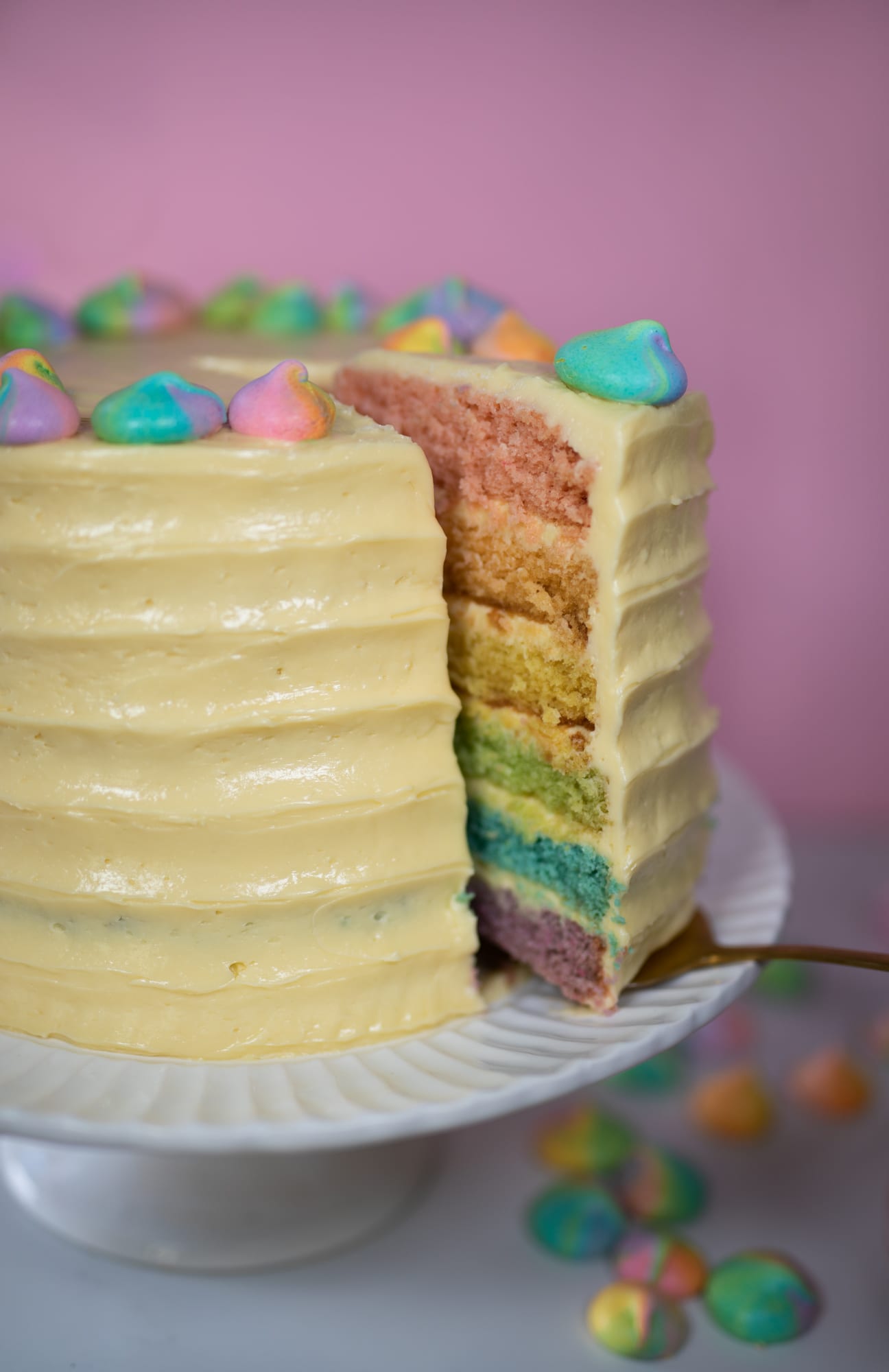 A slice being lifted out of a pastel rainbow cake, showing the rainbow layers