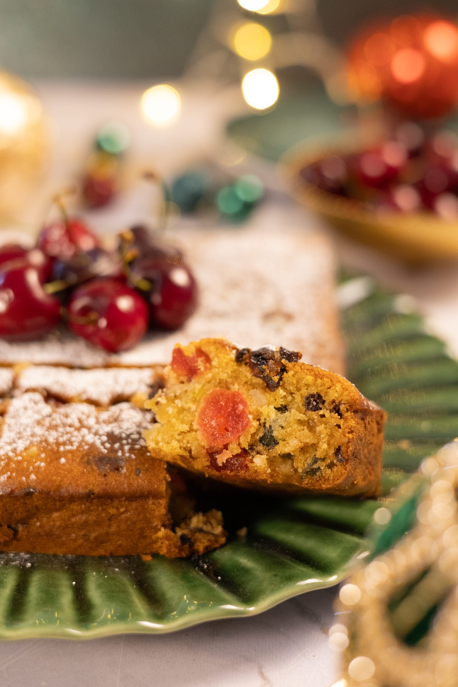 A slice of fruitcake studded with glacé fruit, beside a bowl of cherries