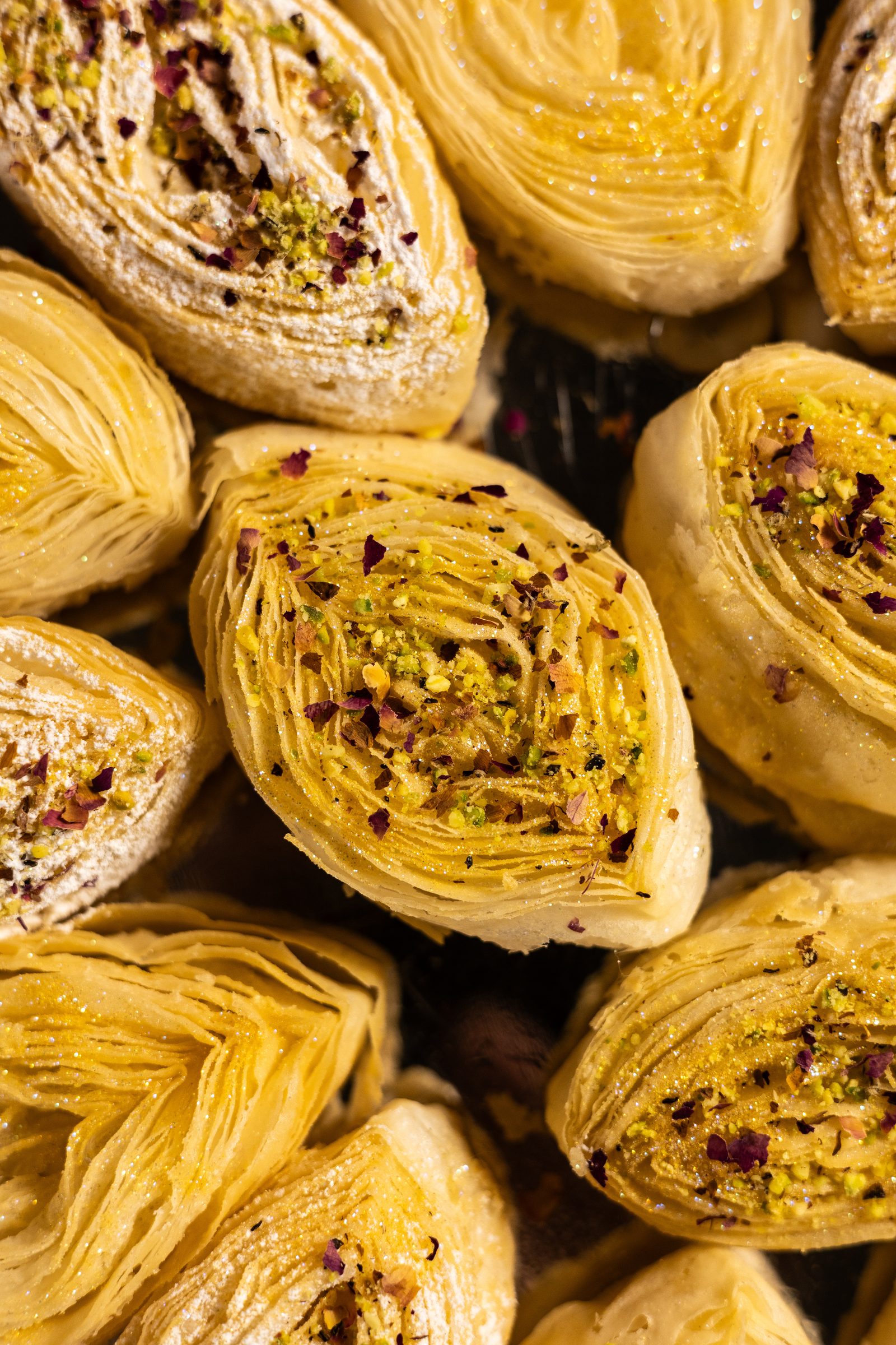 Close-up of banana puri topped with crushed pistachios and rose petals, from above