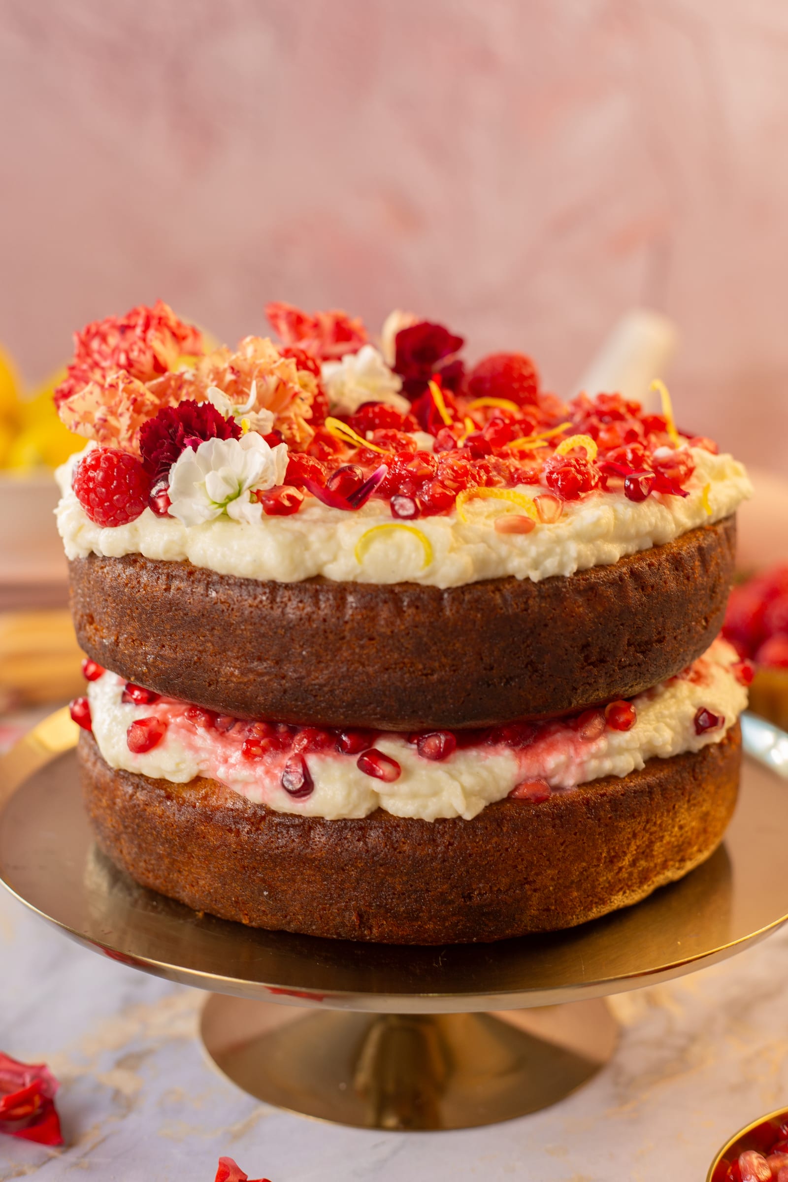 A two-layer lemon, rose and raspberry cake on a gold stand