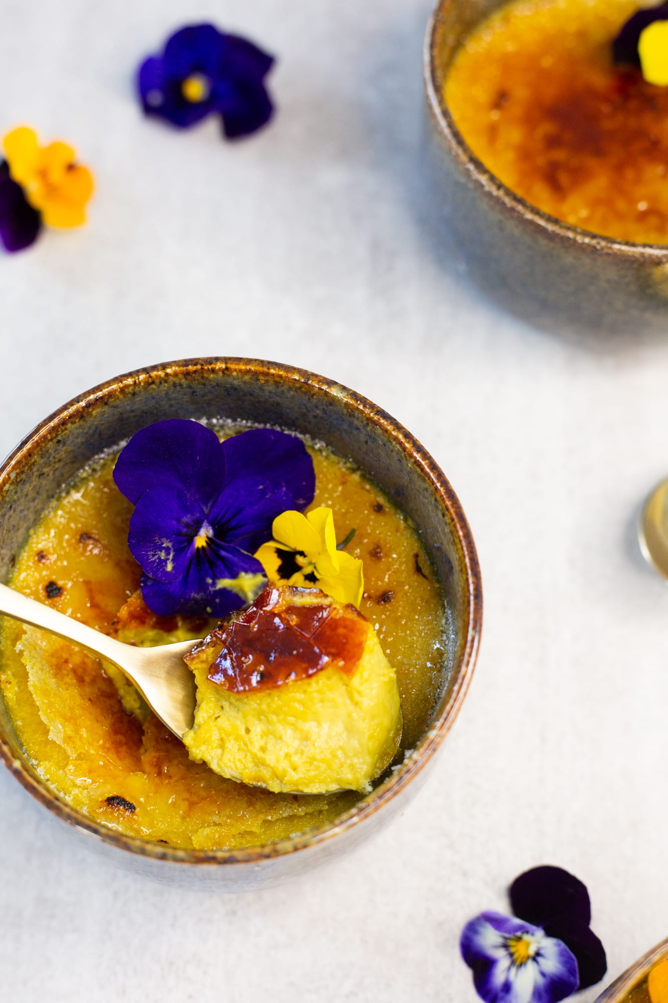 A spoonful of custard lifted from a chai-spiced crème brûlée with a broken top, from above