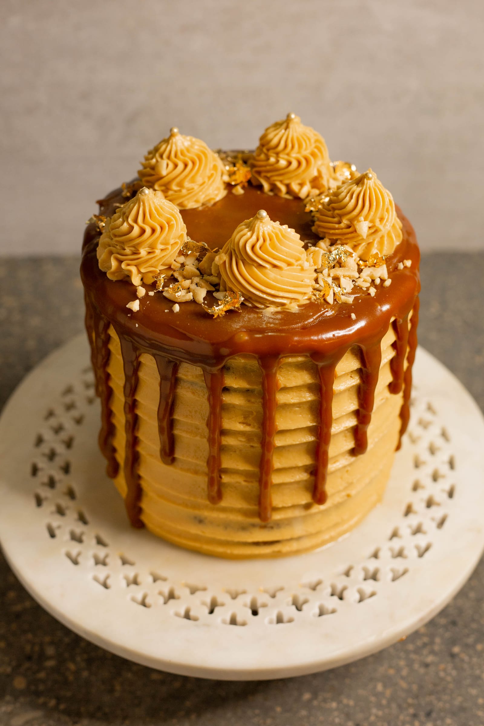 A salted caramel peanut cake with a caramel drip on a white cake stand