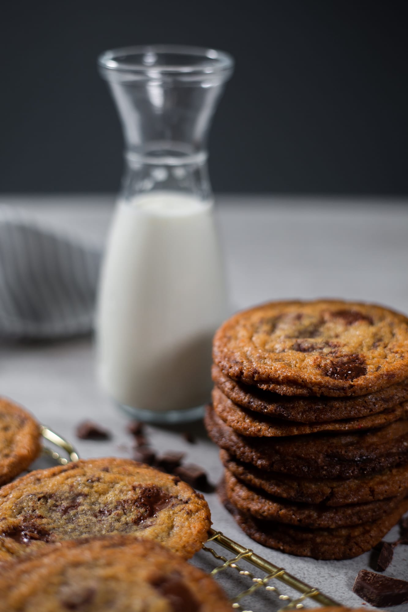 A tall stack of pan banging chocolate chip cookies beside a carafe of milk