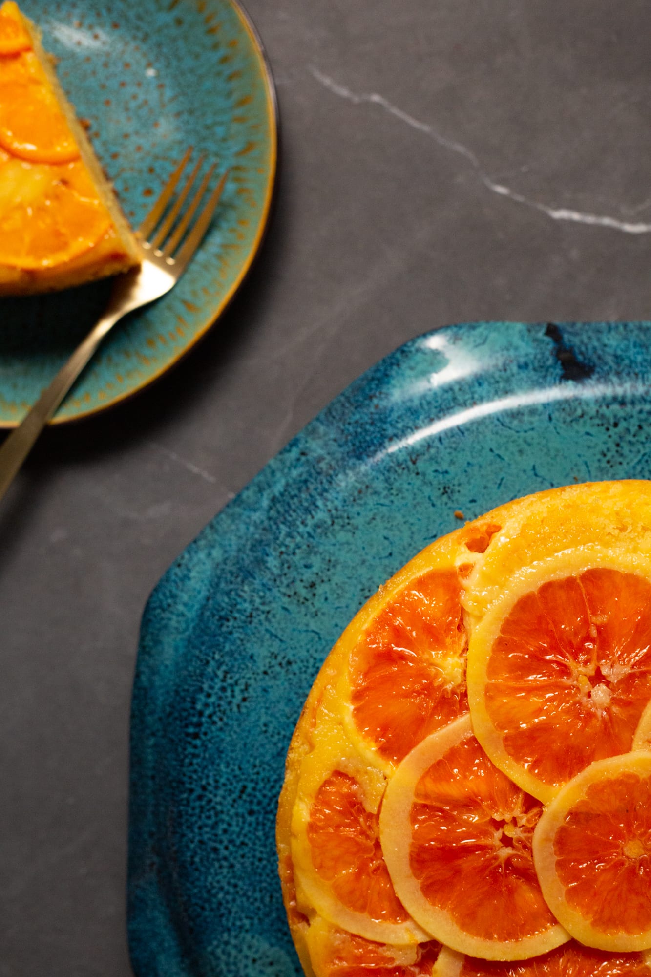 Part of an orange upside down cake beside a plate with a slice and forks, from above