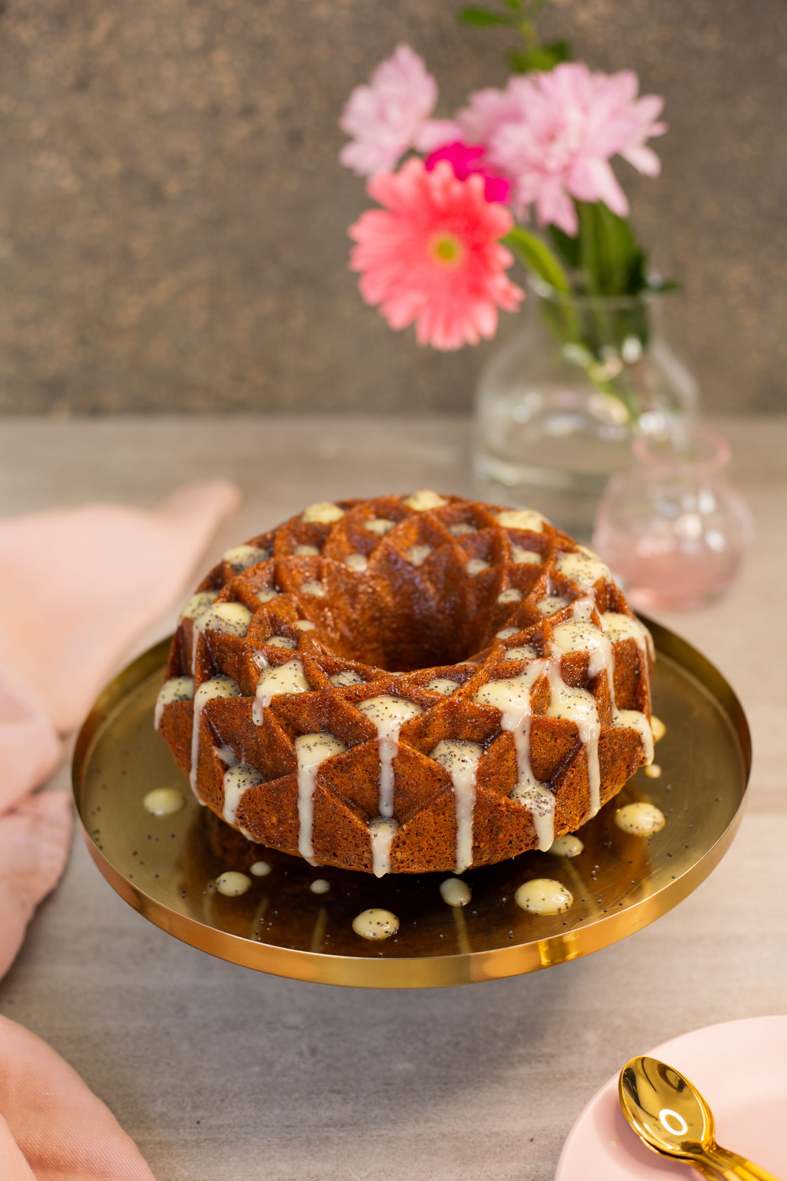White glaze dripping down a lemon, poppyseed and olive oil bundt on a gold stand