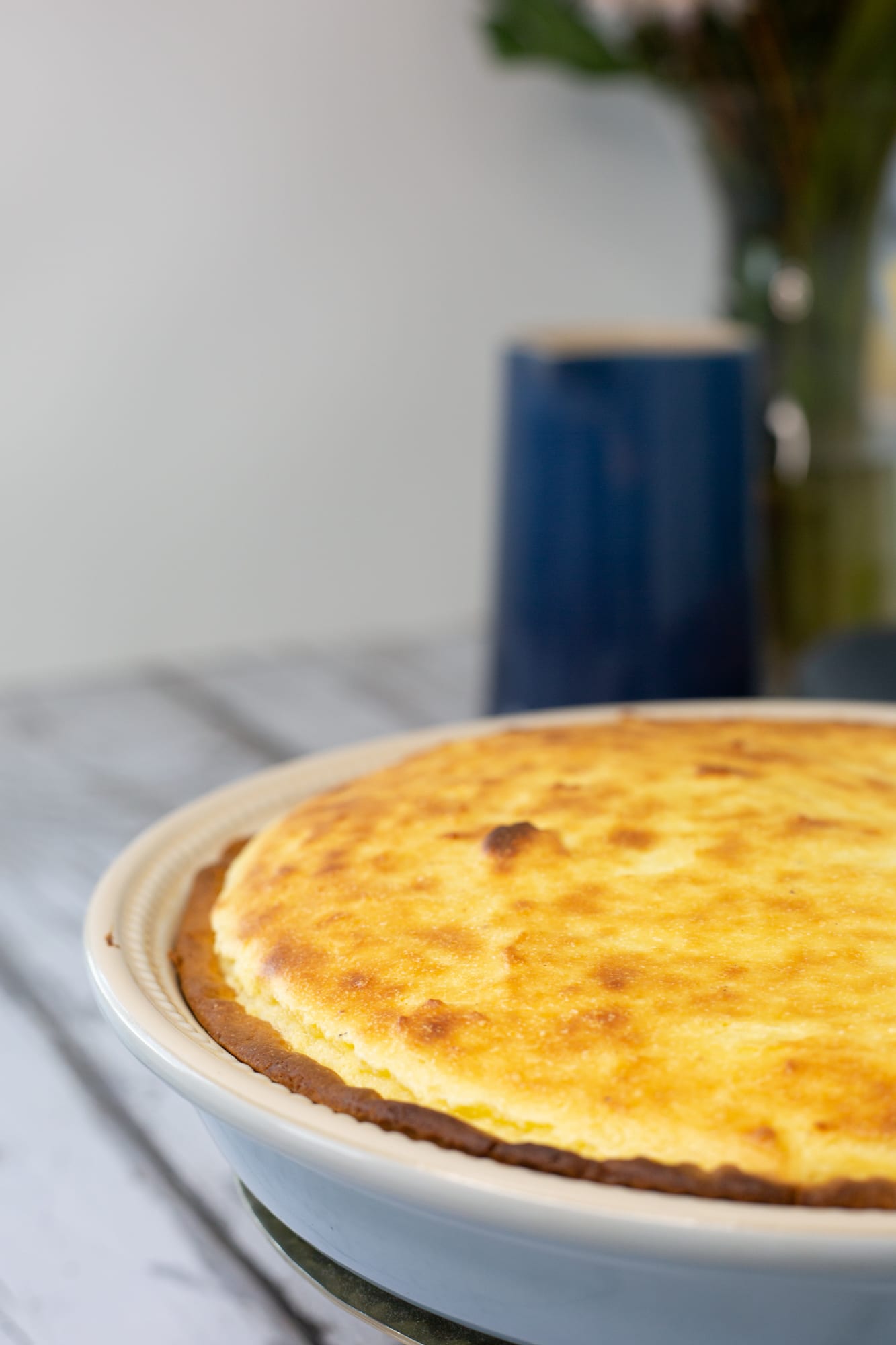 Close-up of a baked melktert before its cinnamon dusting, a blue jug behind
