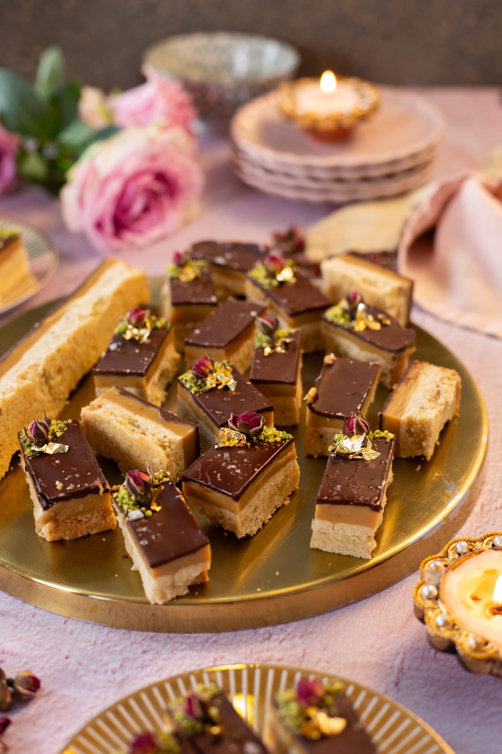 Millionaire's shortbread on a gold platter, with pink roses and a candle behind