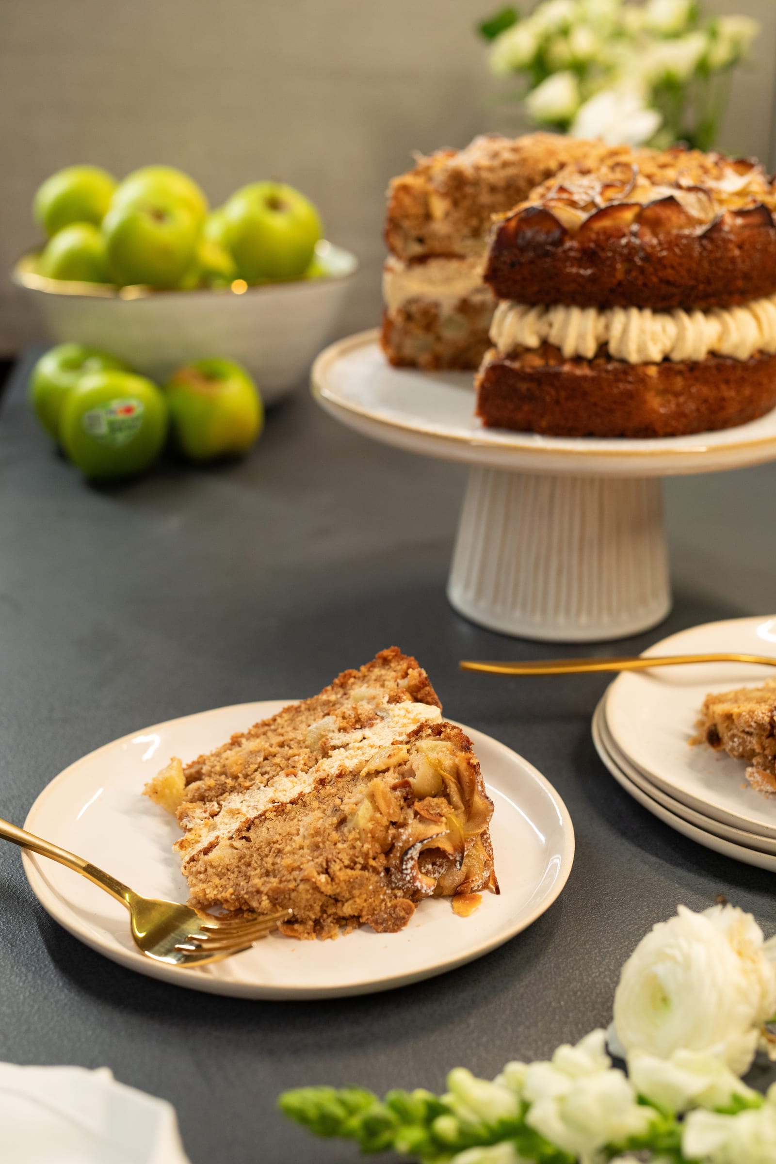 The cut apple crumble cake on its stand behind a slice on a plate