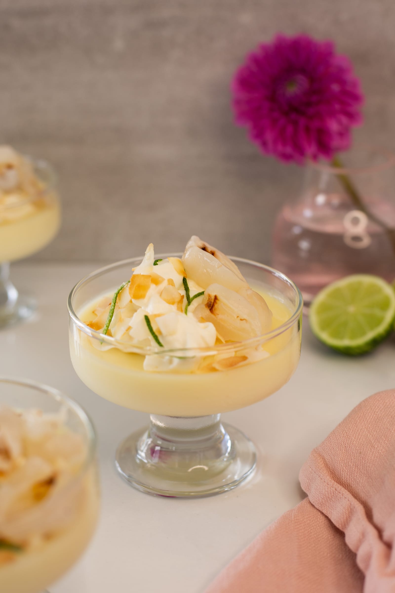 A lime and coconut posset topped with whipped cream, litchi and toasted coconut in a footed glass