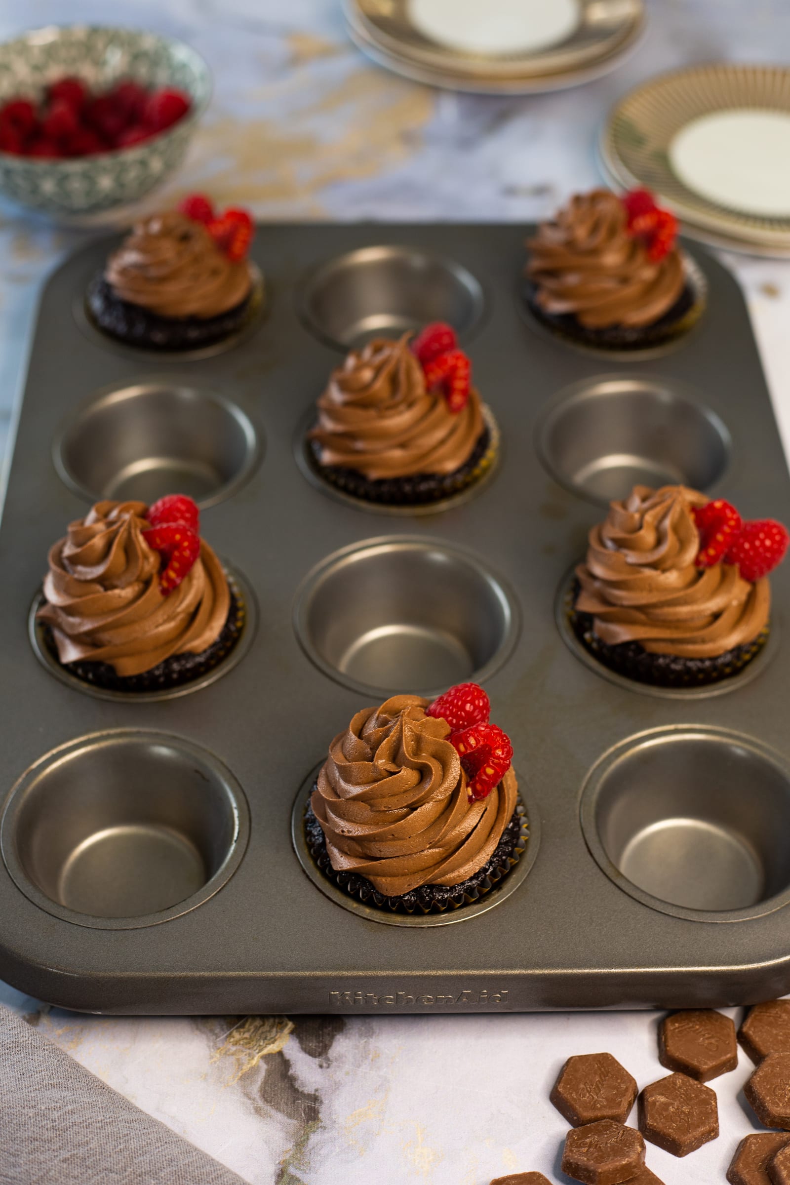 A tin of ultimate triple chocolate cupcakes topped with raspberries and chocolate pieces, from above