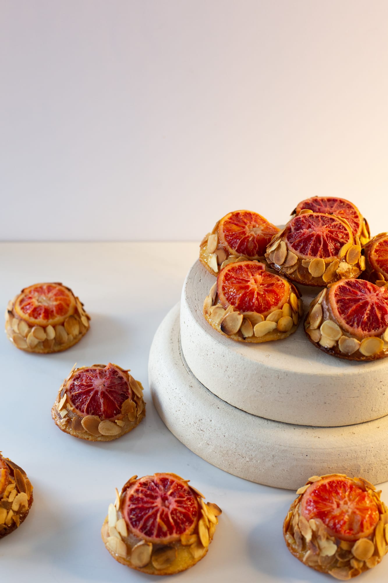 Blood orange and almond tea cakes stacked on a two-tier stone riser, from a low angle