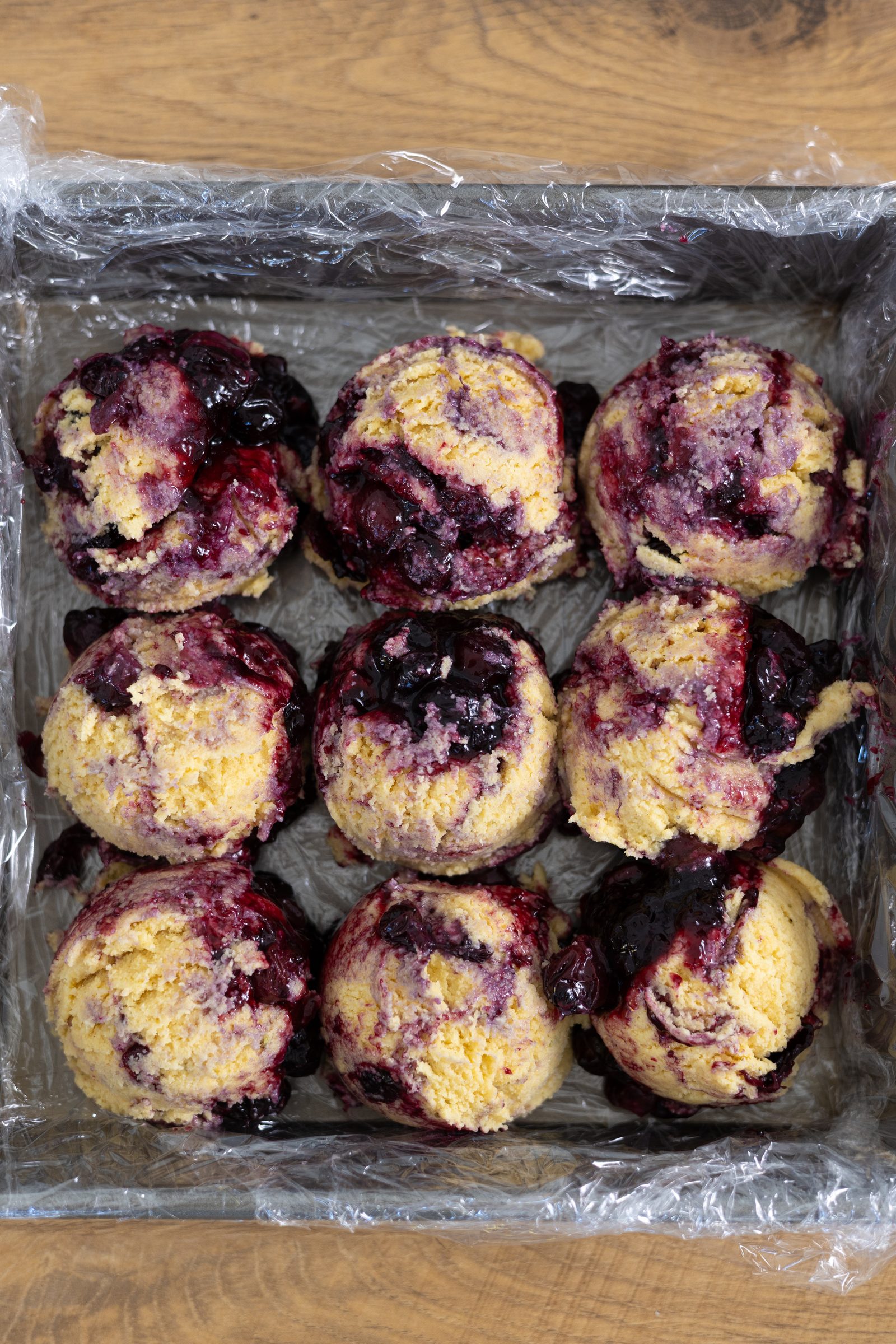 Balls of burfee pressed into a cling-wrapped tray with blueberry compote spooned between them, from above