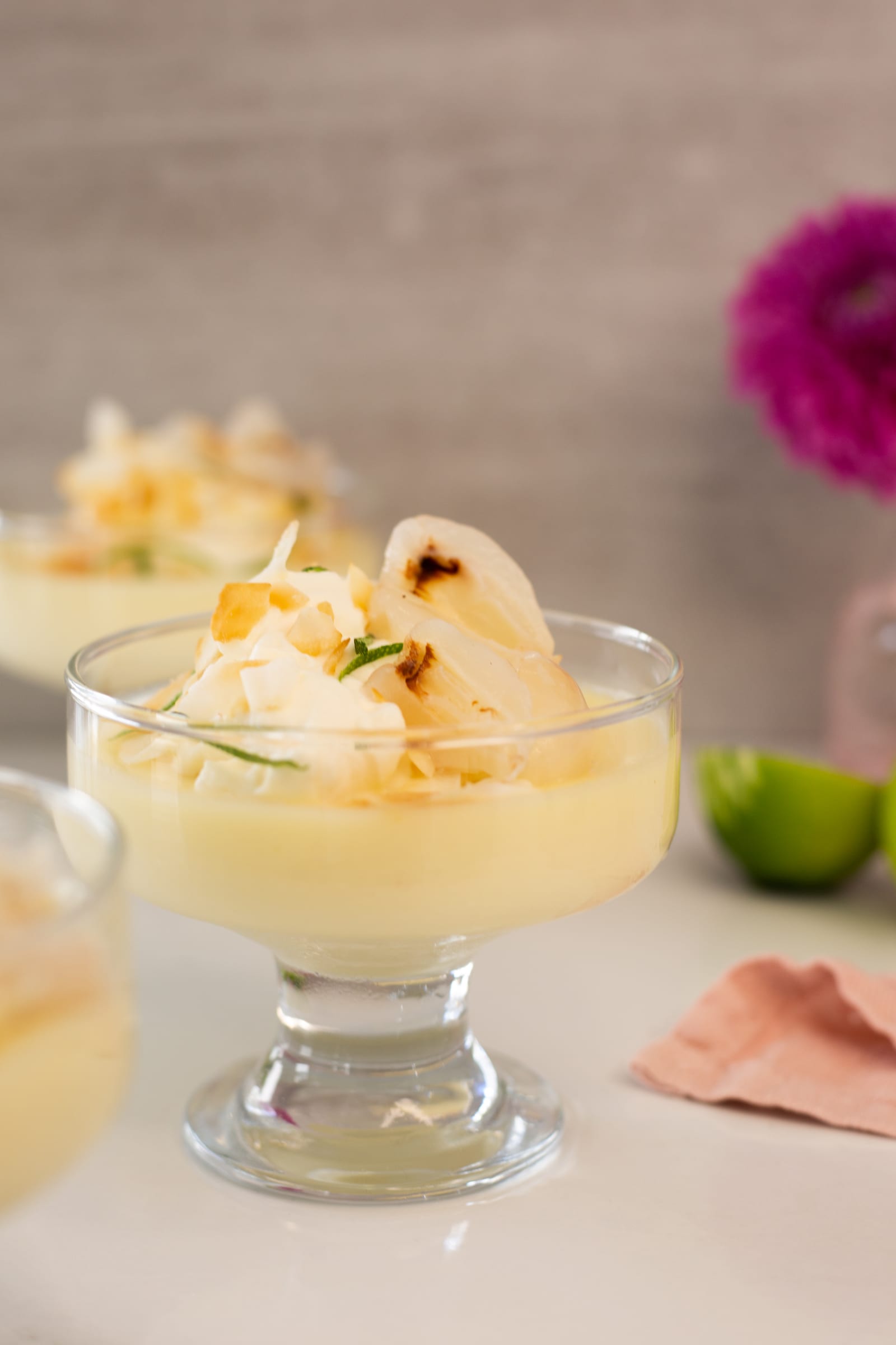 A lime and coconut posset with litchis in a footed glass, a pink dahlia behind