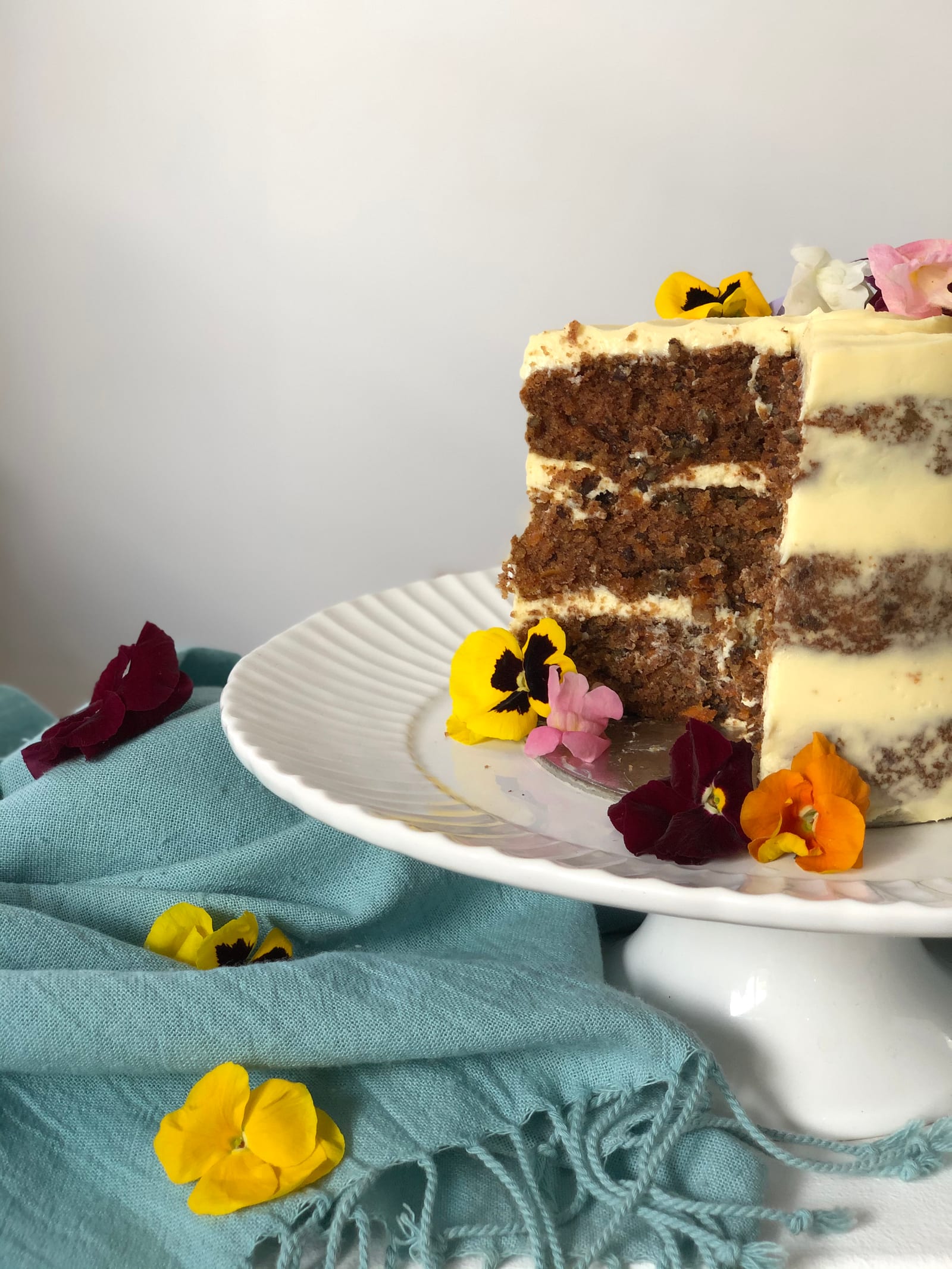 A cut carrot cake on its stand, showing the layers of crumb and icing