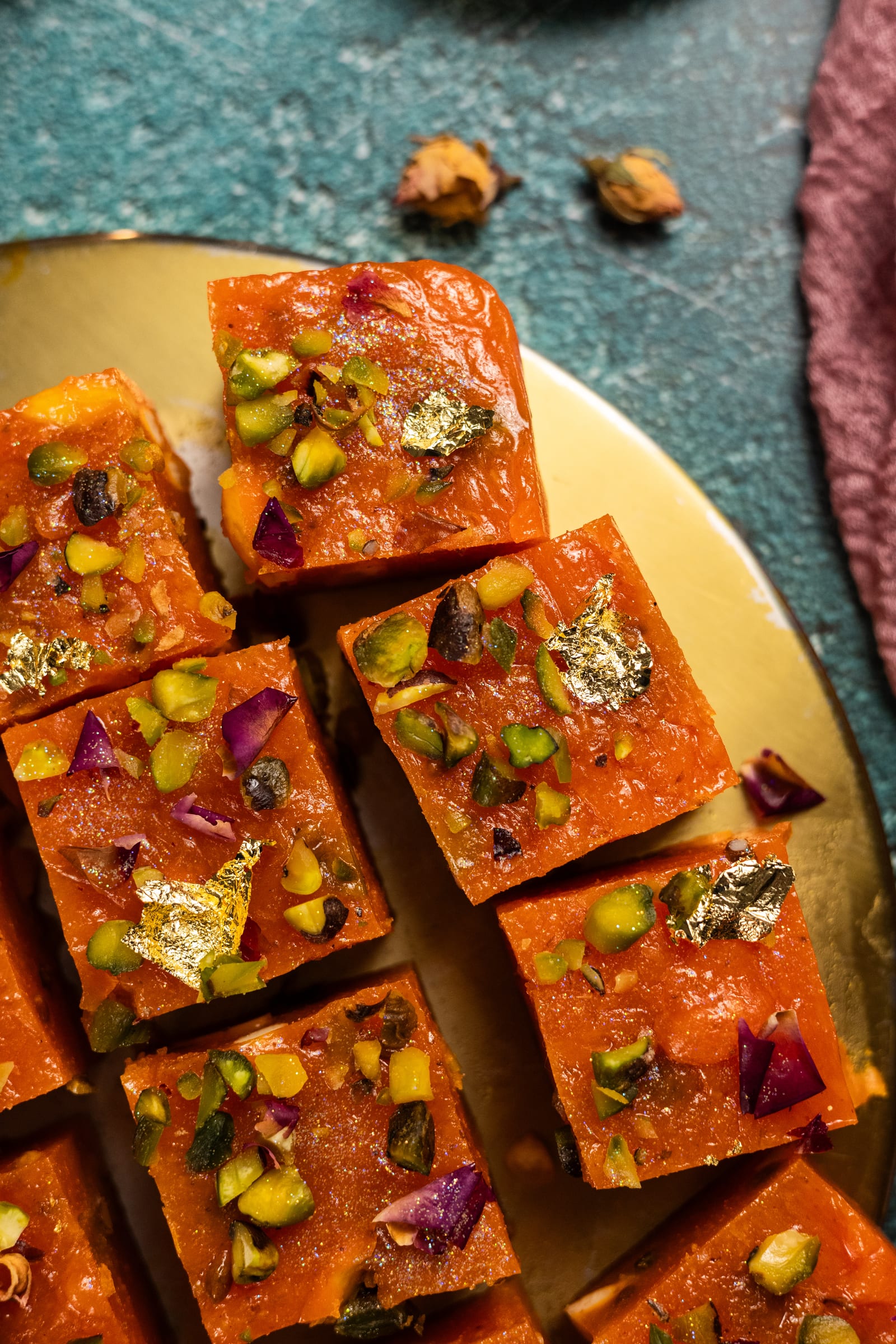 Blocks of halwa topped with pistachios and gold leaf, close up from above