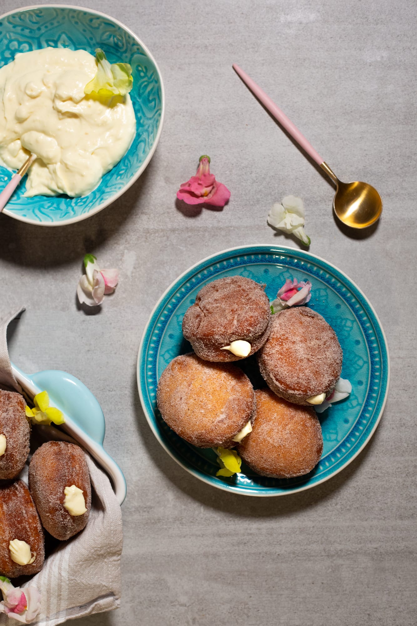 A teal plate of doughnuts filled with milk tart mousse beside a bowl of mousse and spoons, from above