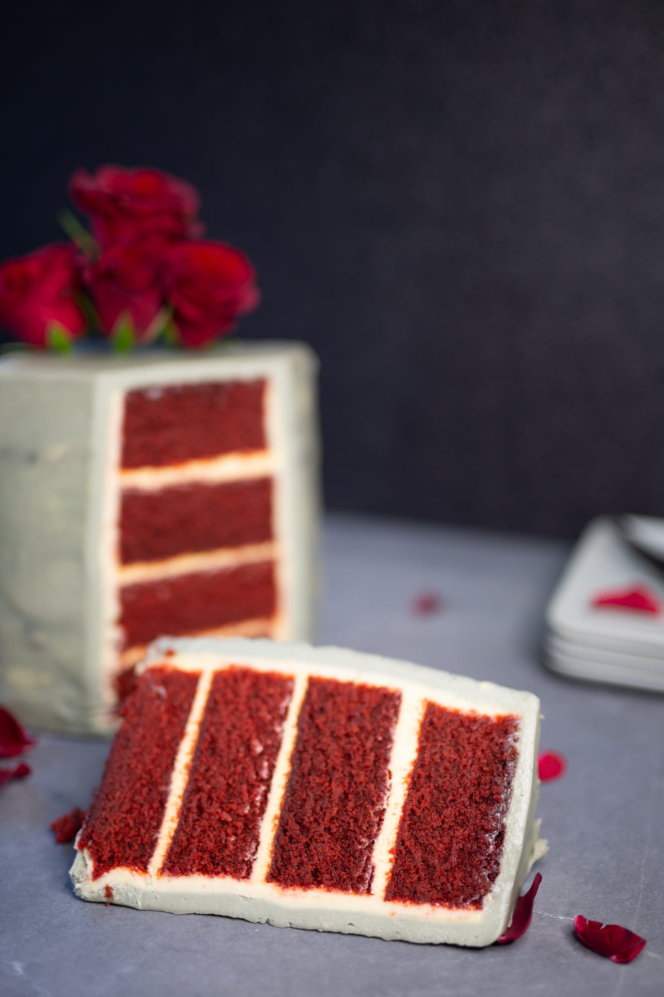 A cut decadent red velvet cake showing its four red layers, a slice in front