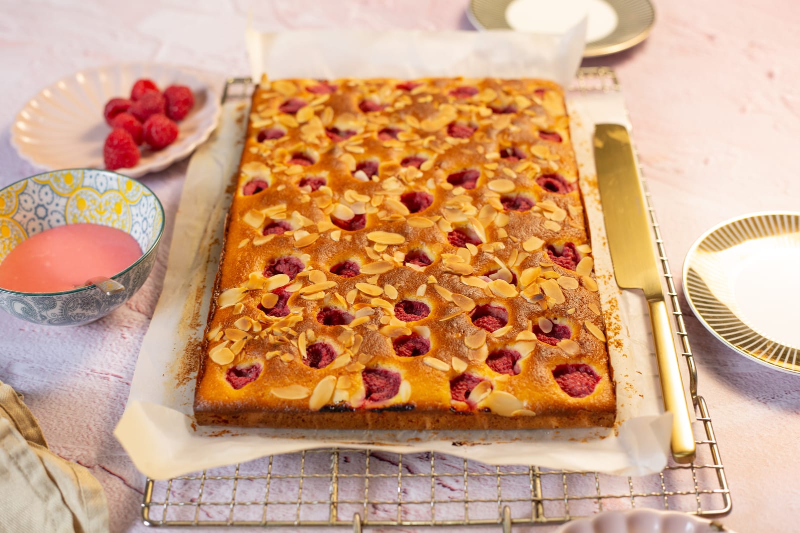 A raspberry, almond and olive oil snack cake on a wire rack, scattered with flaked almonds