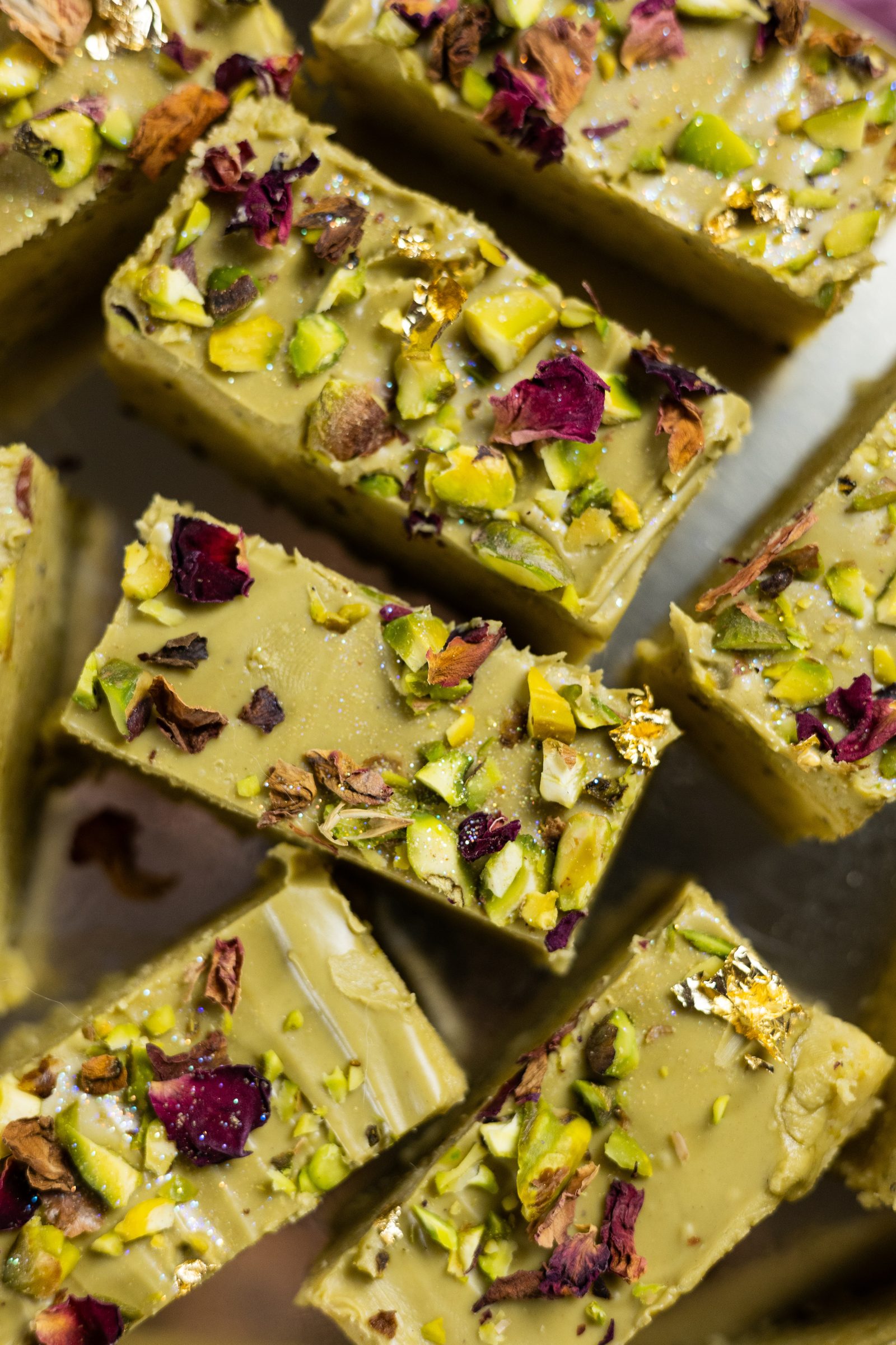 Close-up of pistachio burfee squares with rose petals, pistachios and gold leaf, from above