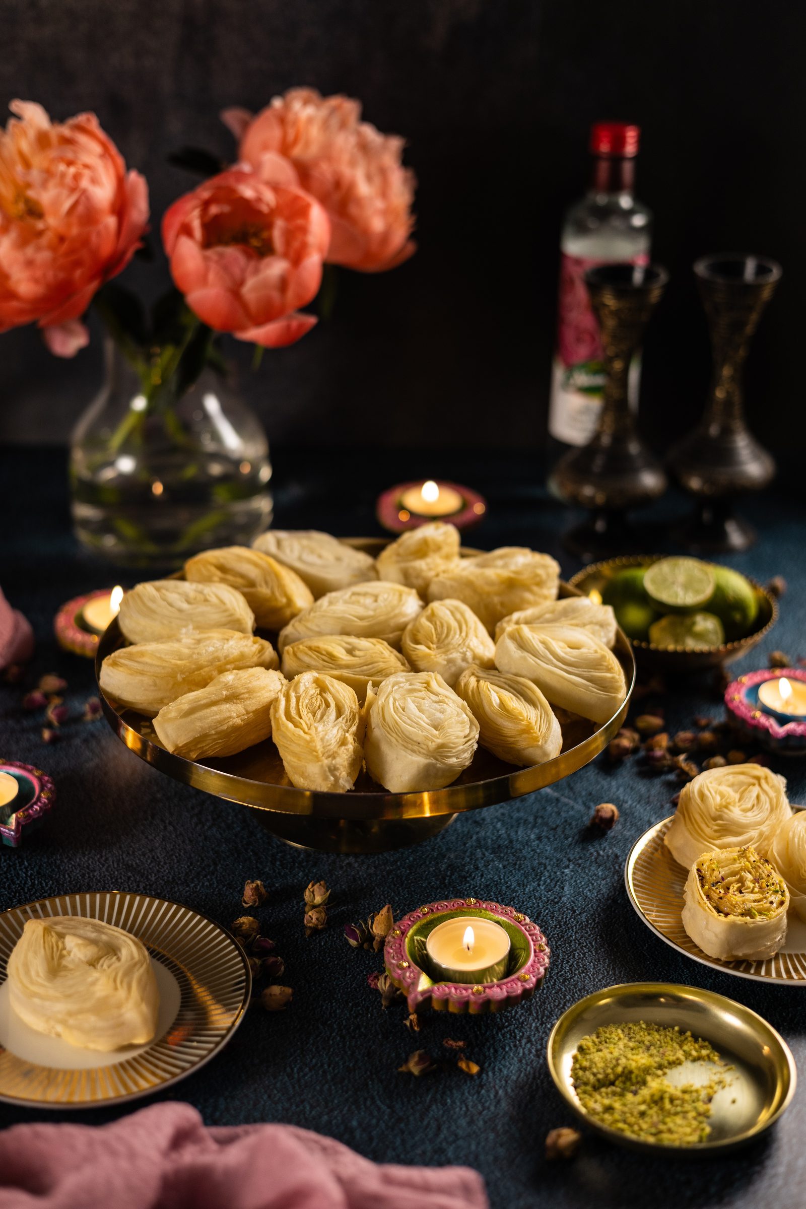 A Diwali table with banana puri piled on a gold cake stand, peonies and diyas