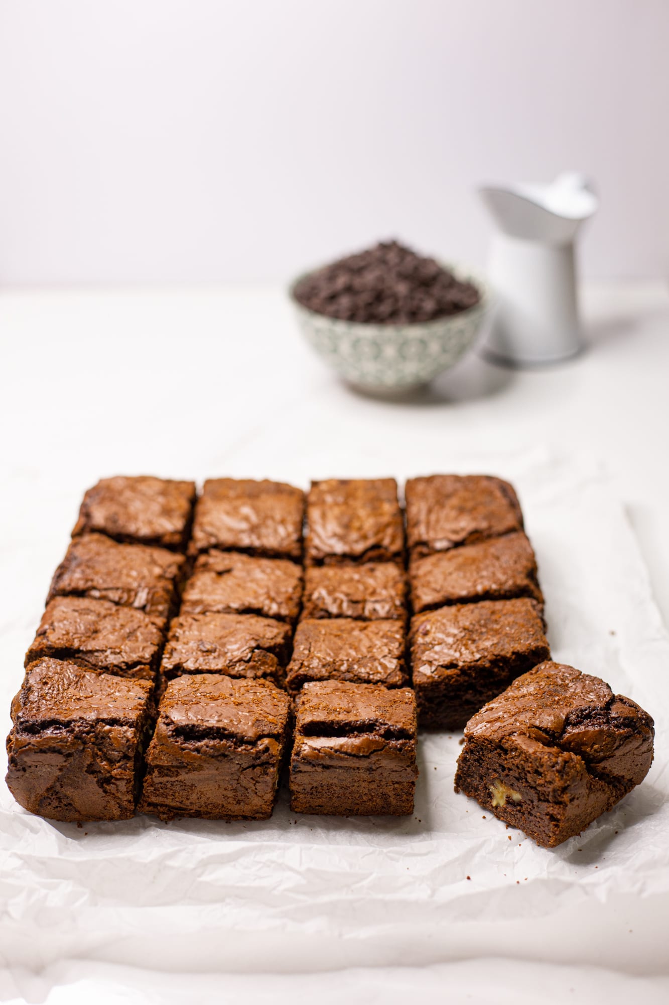 Chocolate brownies cut into squares with a bowl of chocolate chips and a small white jug behind