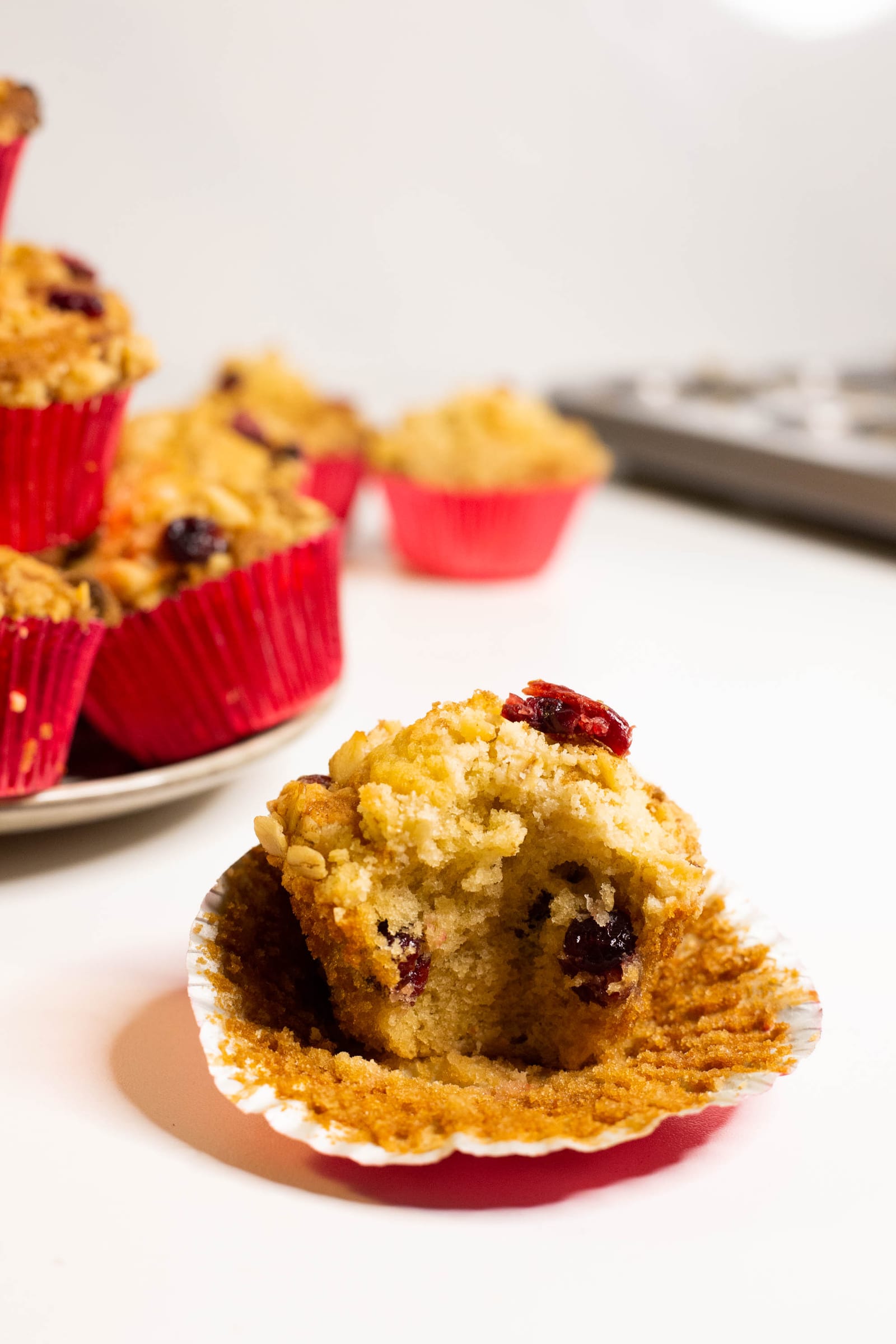A cranberry crumble muffin broken open to show the cranberries, its red case peeled back