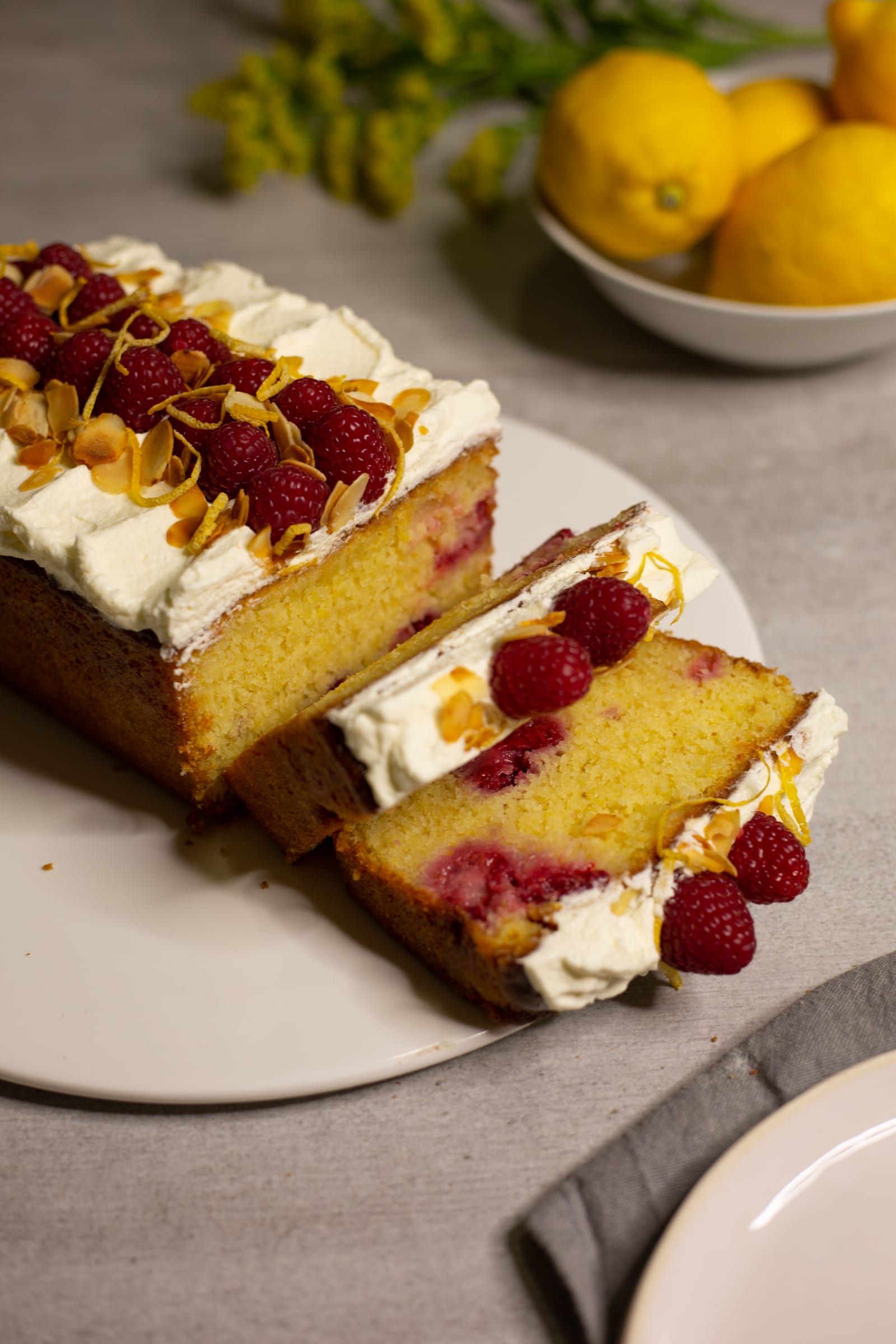 A gluten-free almond, raspberry and lemon loaf with slices fanned out, lemons behind