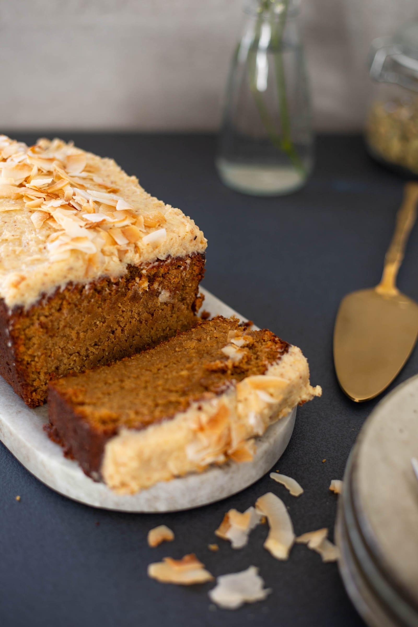 A cut gluten-free coconut loaf with a slice falling forward, coconut crumbs around it