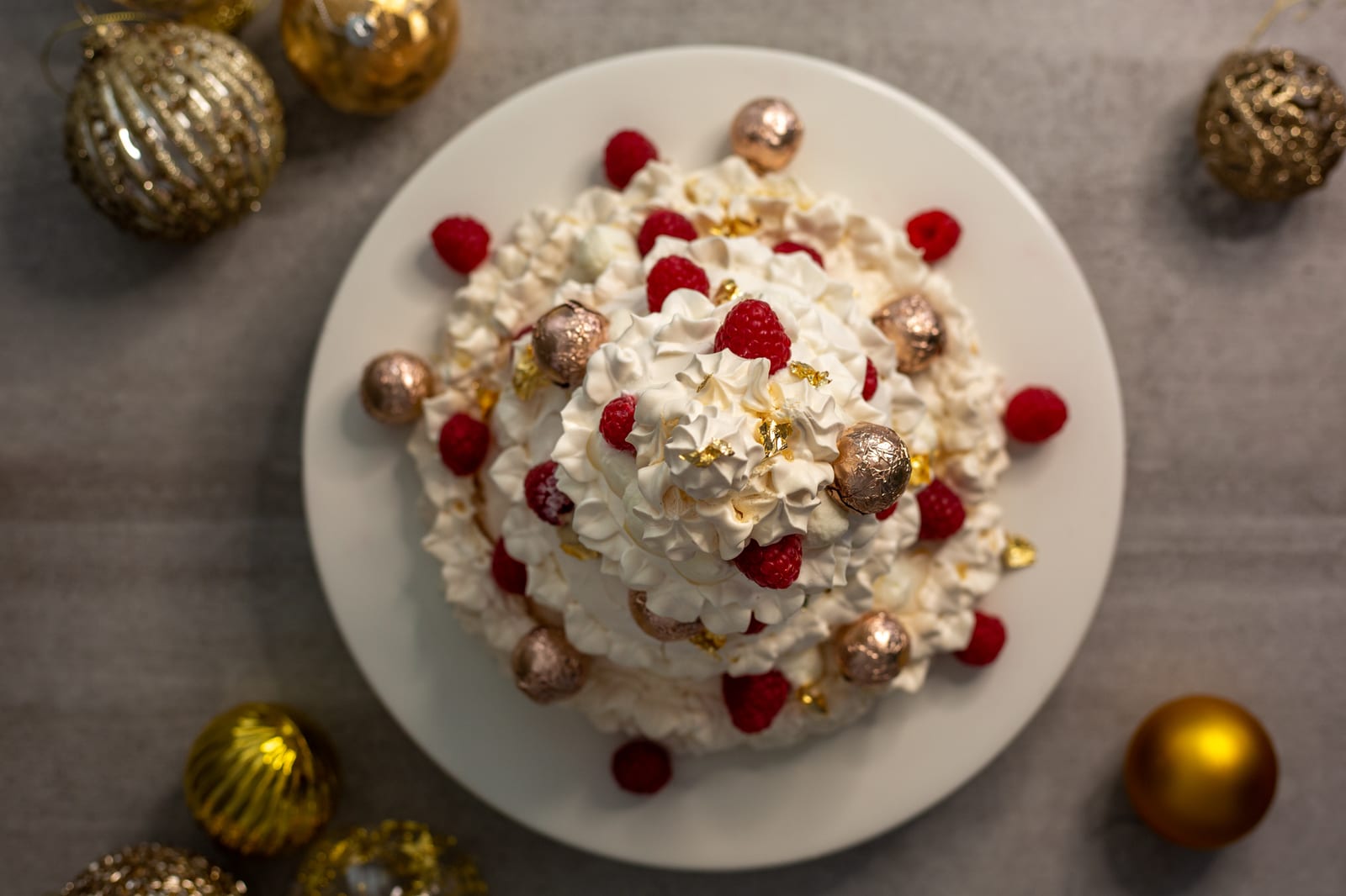 A Christmas tree pavlova on its plate surrounded by gold baubles, from above