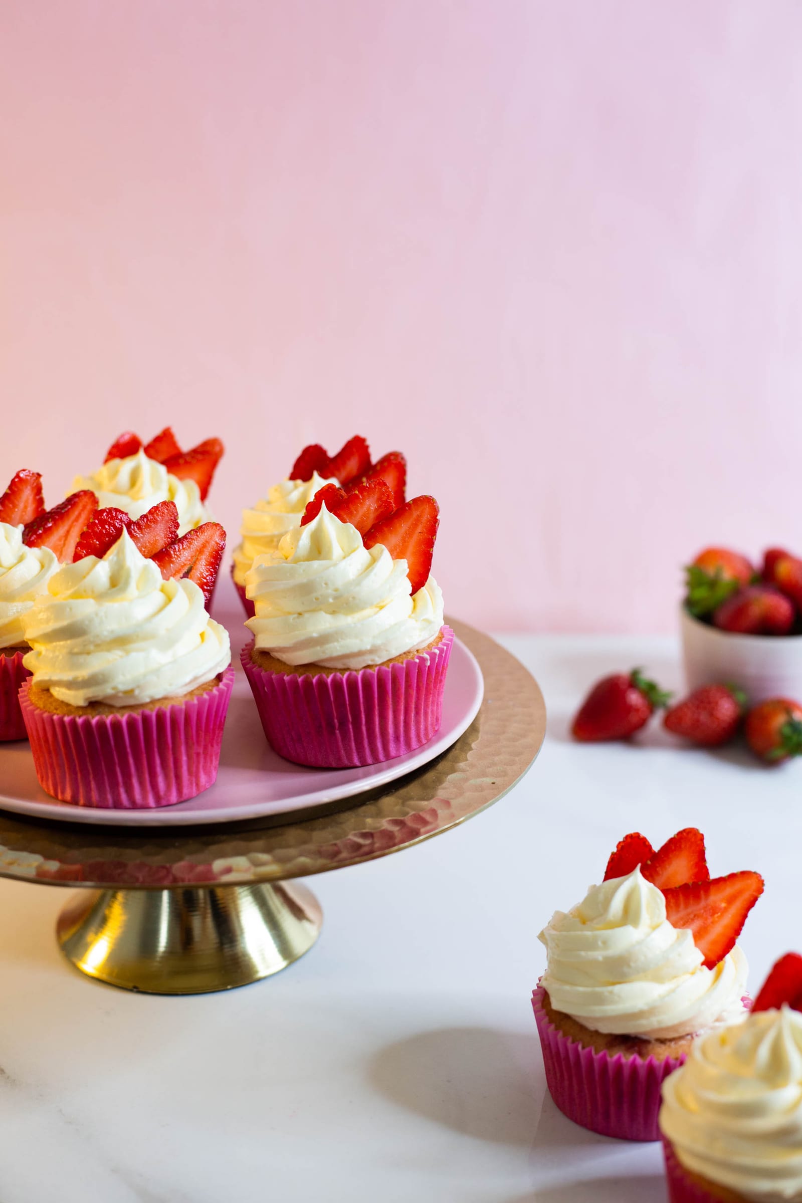 Strawberry and white chocolate cupcakes on a gold cake stand, more in front