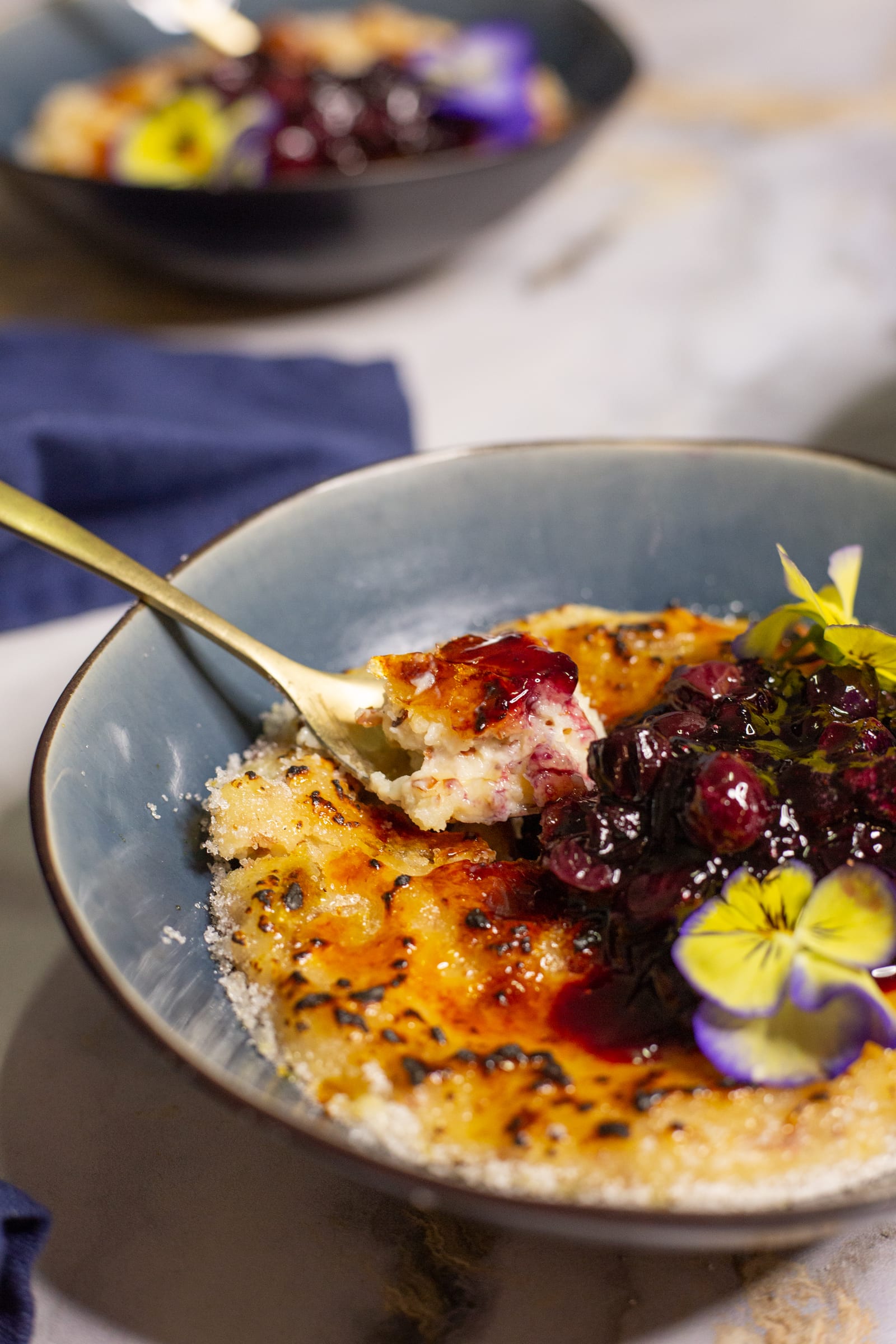 A spoon dug into a kheer brûlée, showing the creamy rice under the caramelised top