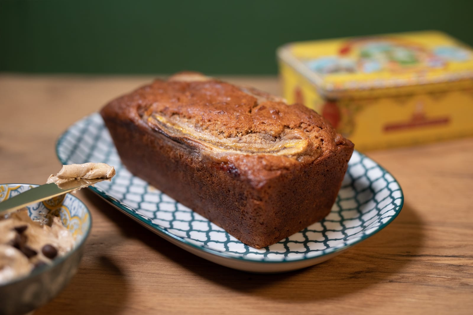 A whole banana and pecan nut bread on a blue and white dish with a bowl of whipped butter