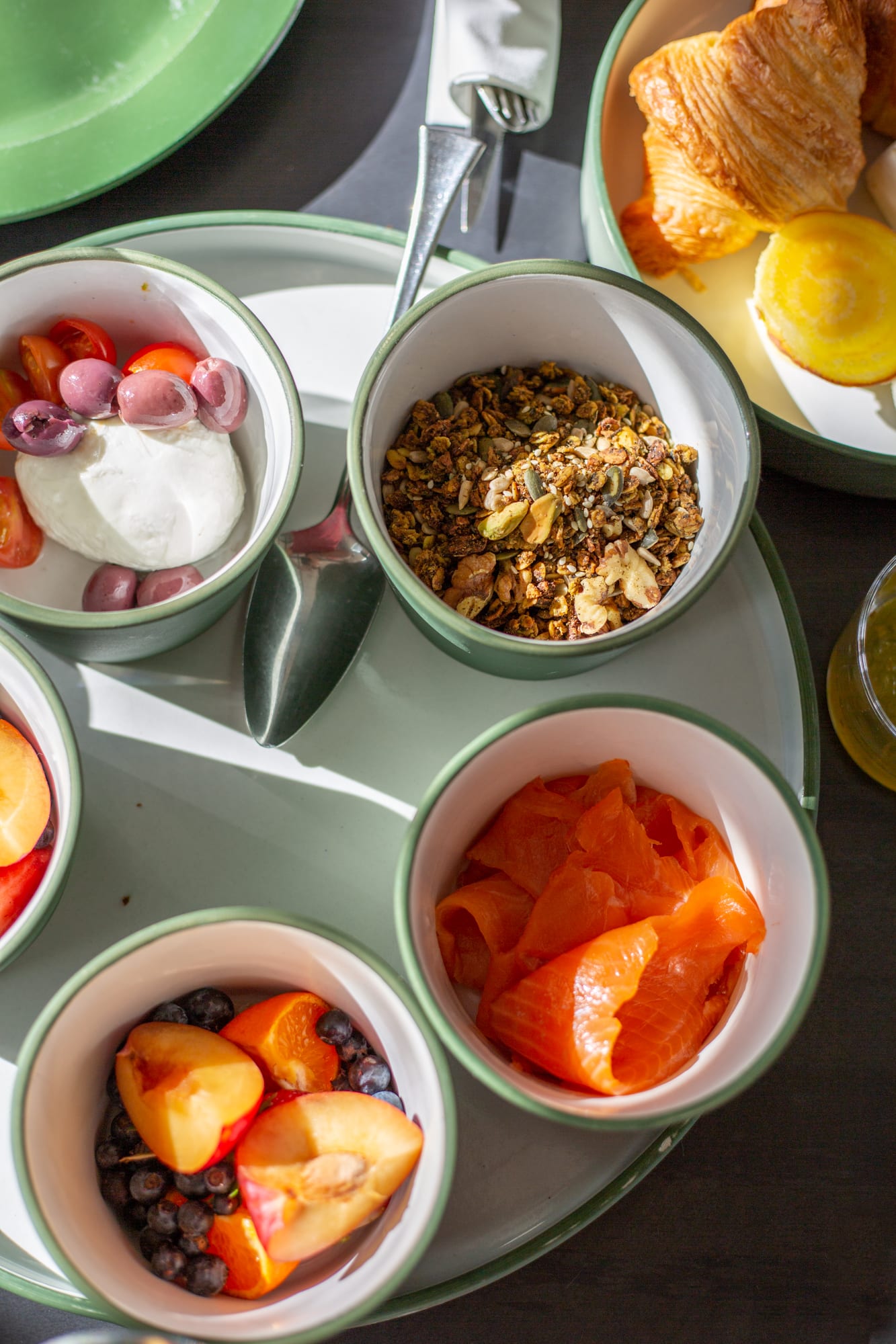 Breakfast at Babel from above: burrata with tomatoes and olives, granola, smoked salmon, and stone fruit with blueberries, beside a croissant