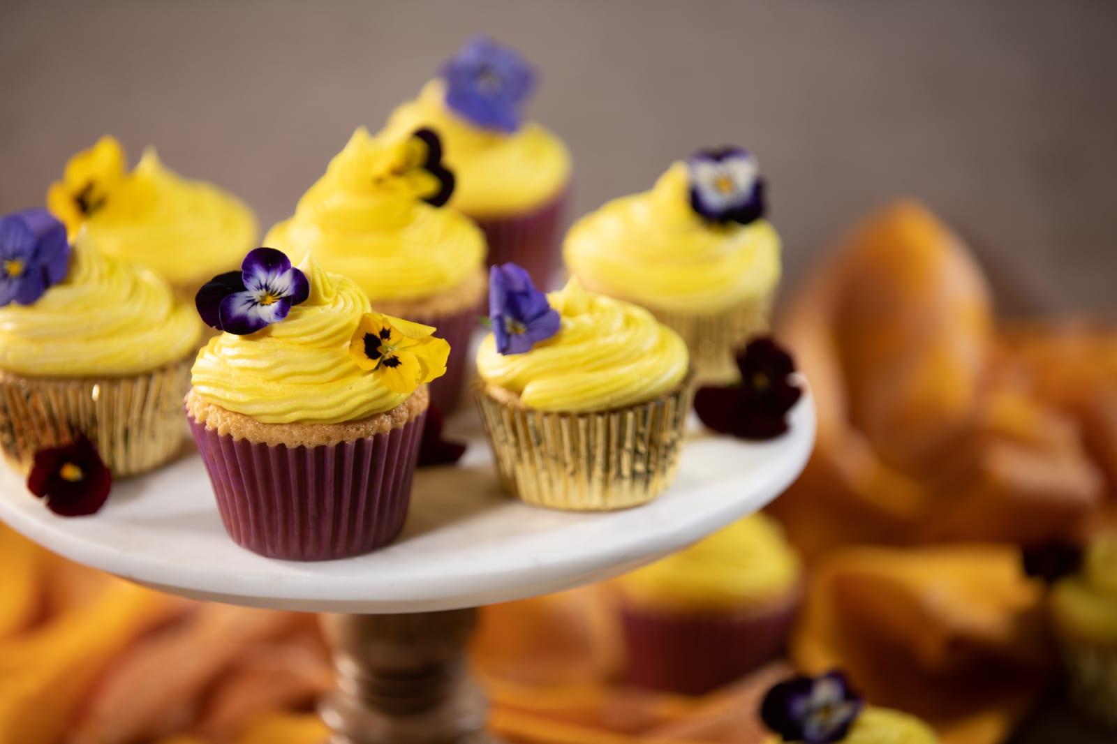 Vanilla cupcakes with yellow buttercream and edible pansies on a cake stand