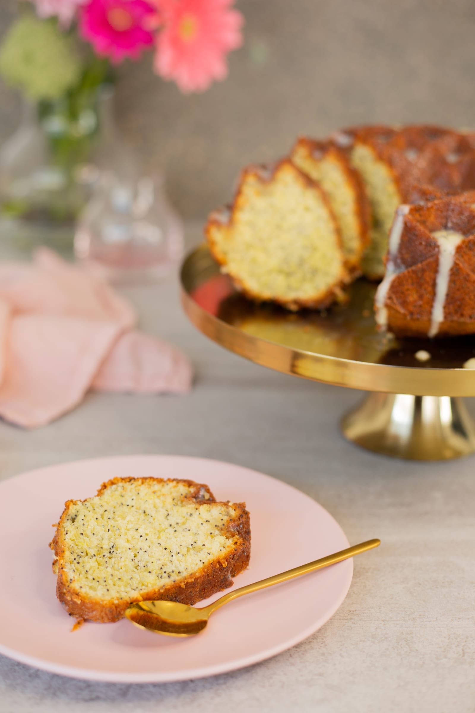 A slice of lemon, poppyseed and olive oil bundt on a pink plate with a gold fork