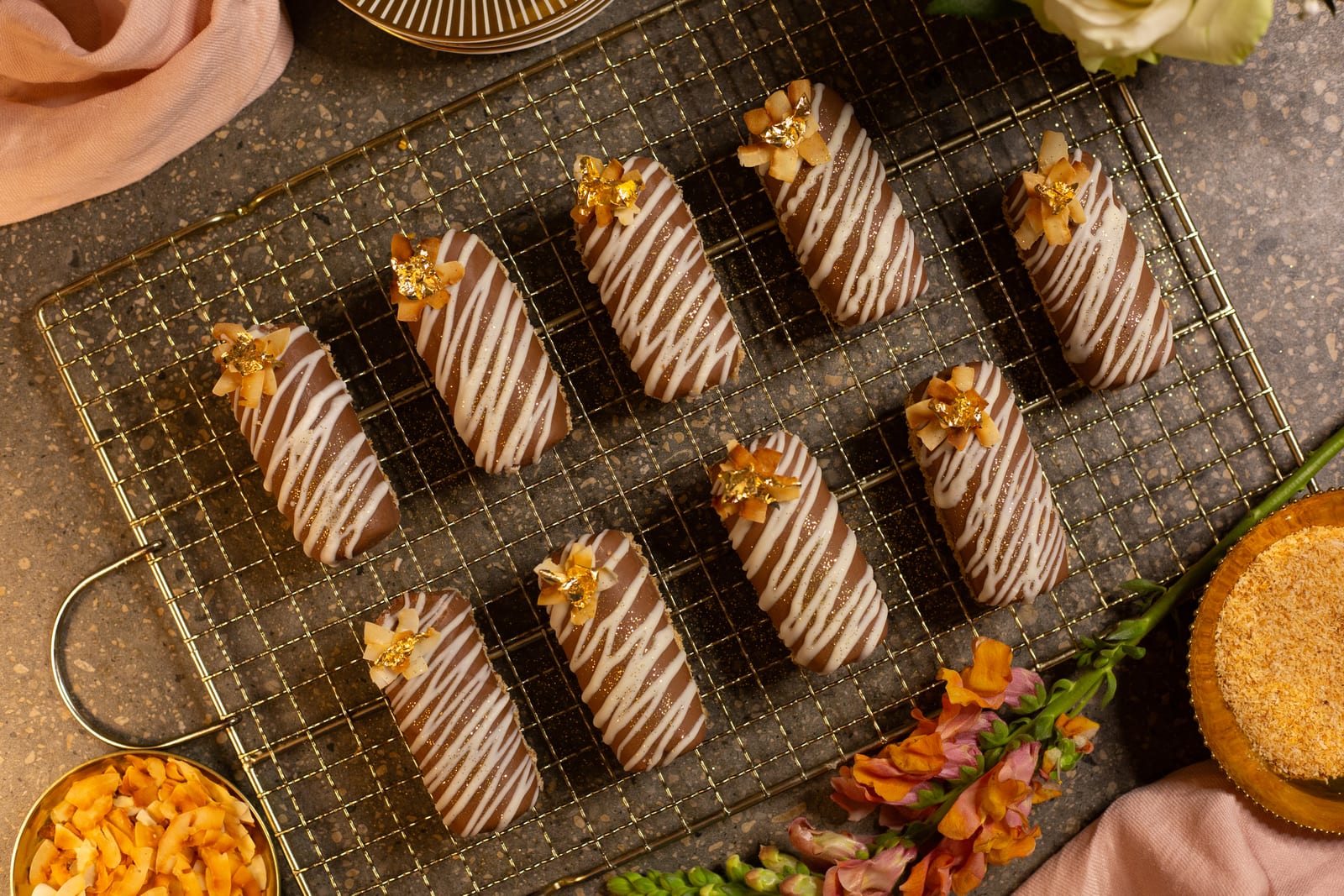 Coconut, caramel and chocolate logs on a gold wire rack, drizzled with white chocolate and topped with gold leaf