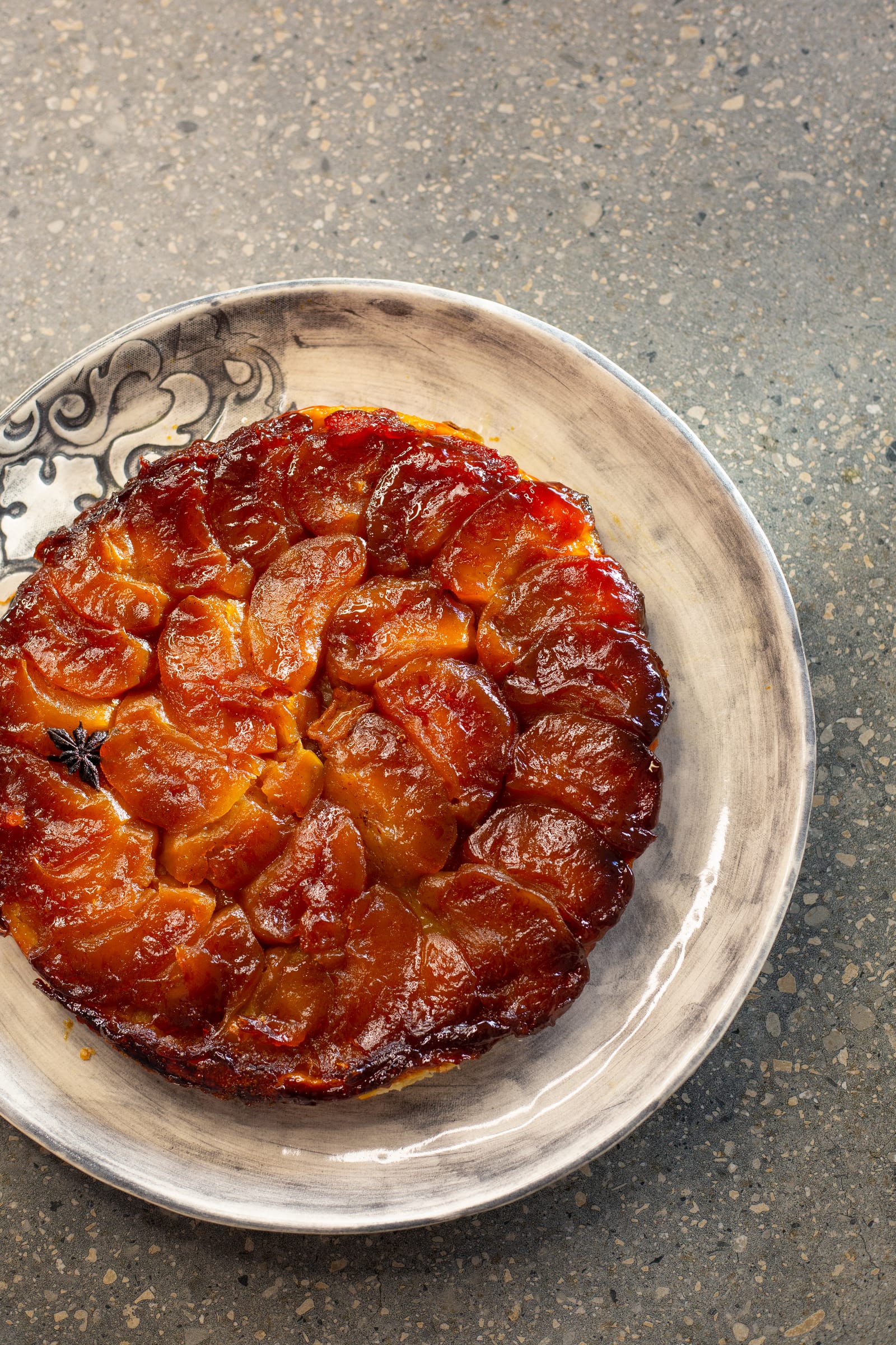 A whole apple tarte tatin on a scroll-rimmed plate