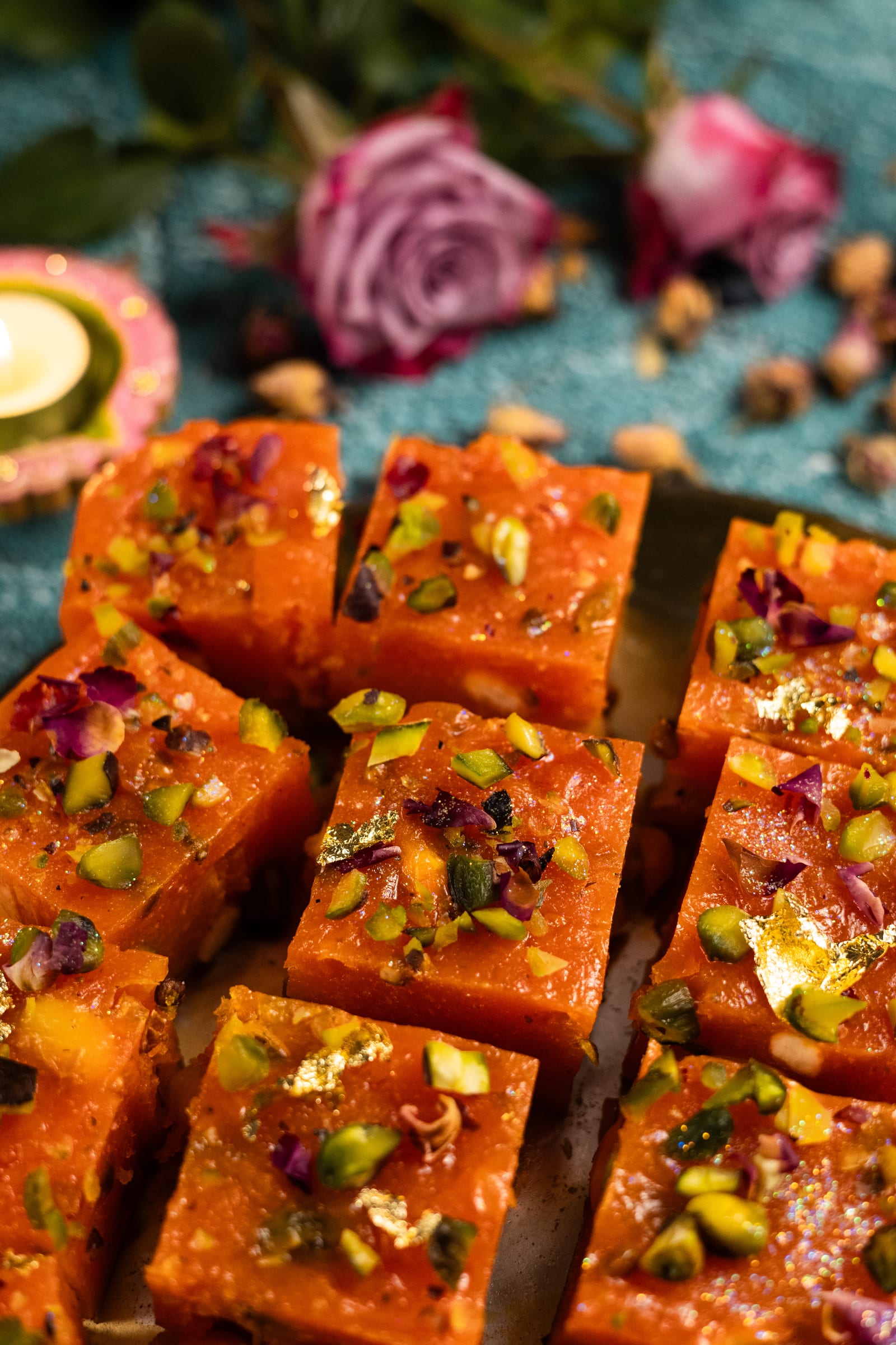 Cut blocks of halwa on a gold board with a pink rose behind, from a low angle