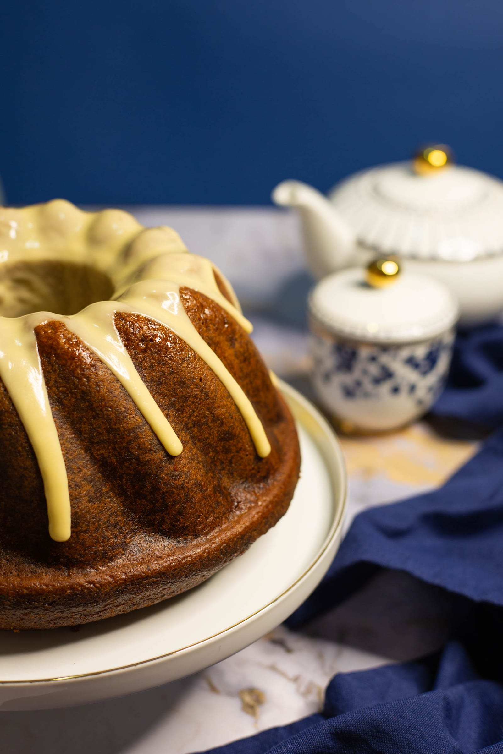 Close-up of a glazed rooibos and honey bundt on its stand, a white teapot behind