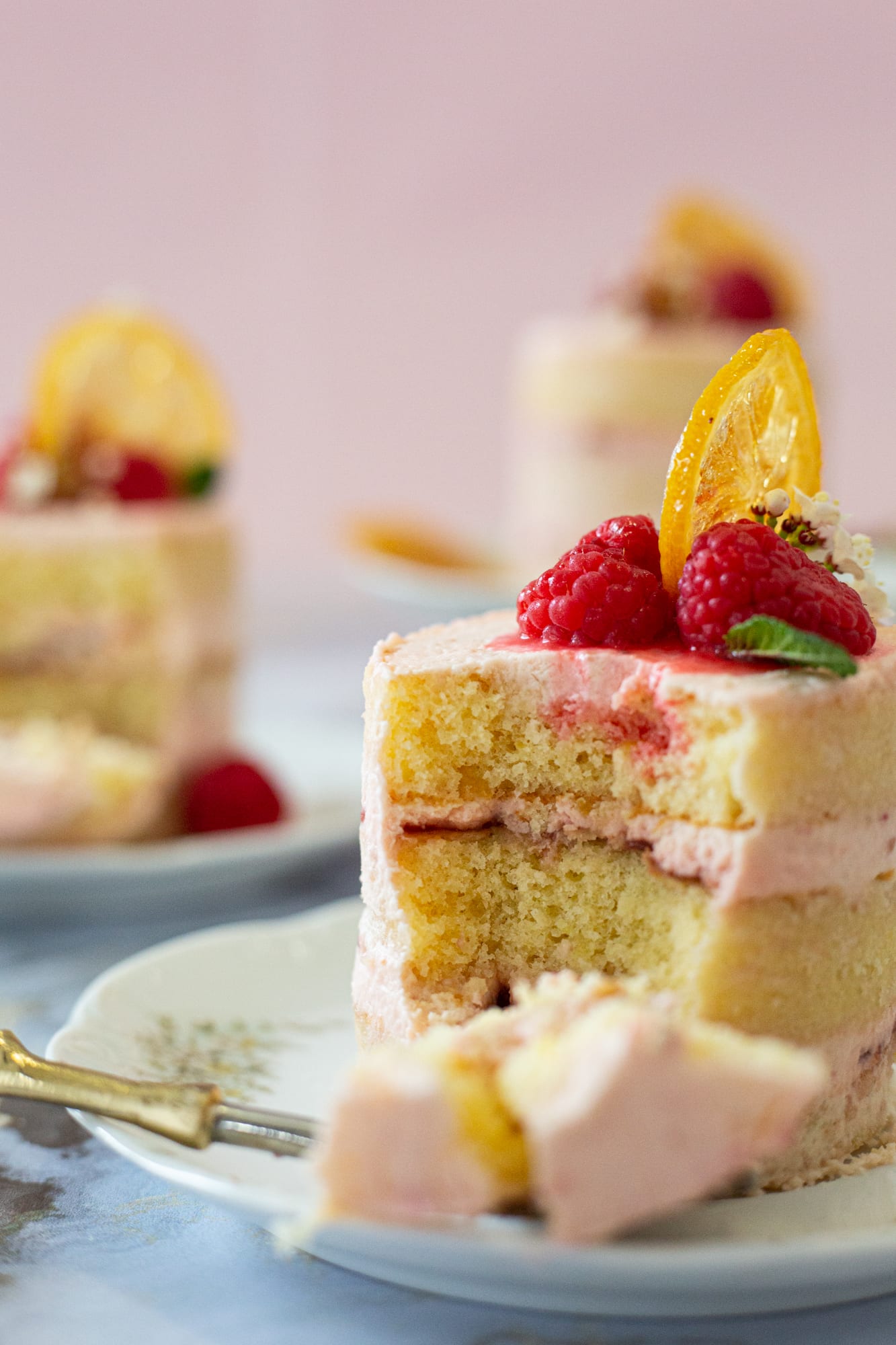 A cut raspberry and lemon mini cake showing its layers, a forkful beside it