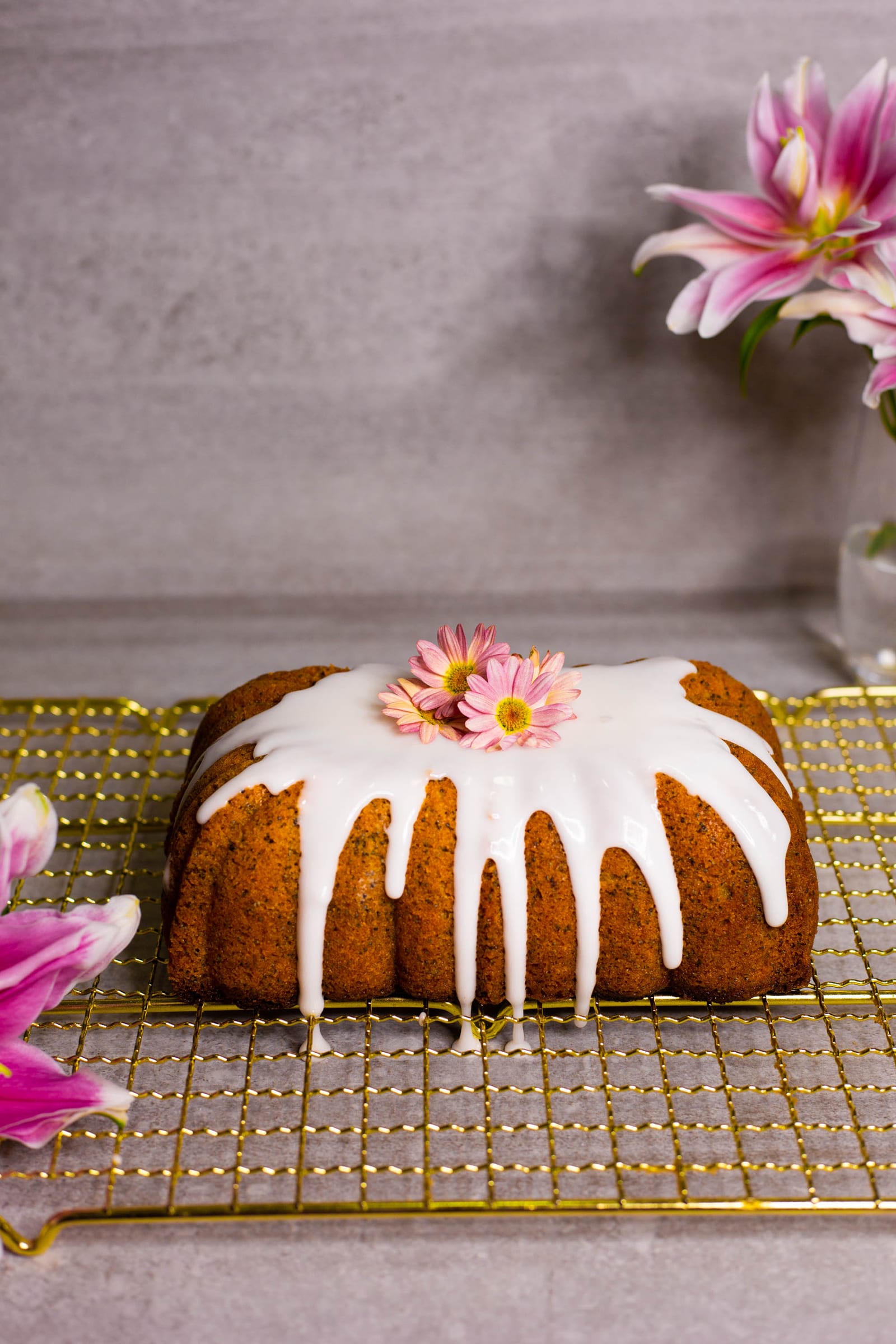 A glazed gluten-free lemon and poppyseed loaf with a pink daisy on top, from the side