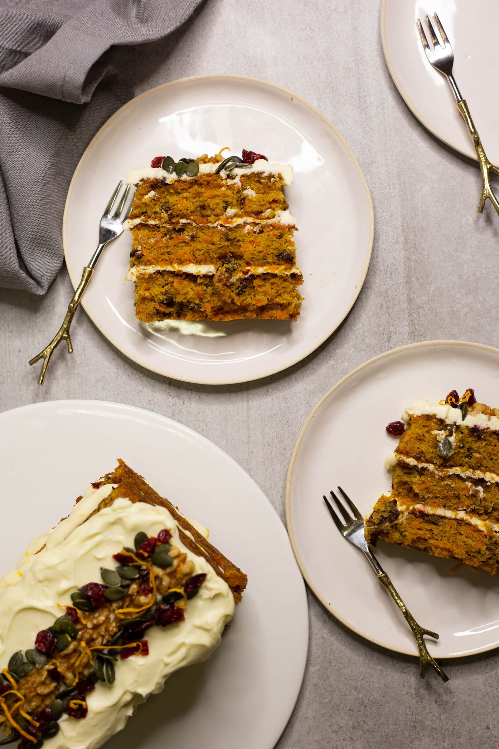 Slices of carrot cake on plates with forks beside the rest of the cake, from above