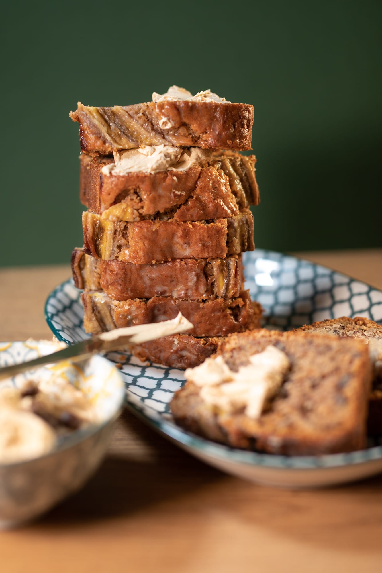 A tall stack of buttered slices of banana and pecan nut bread beside a bowl of whipped butter