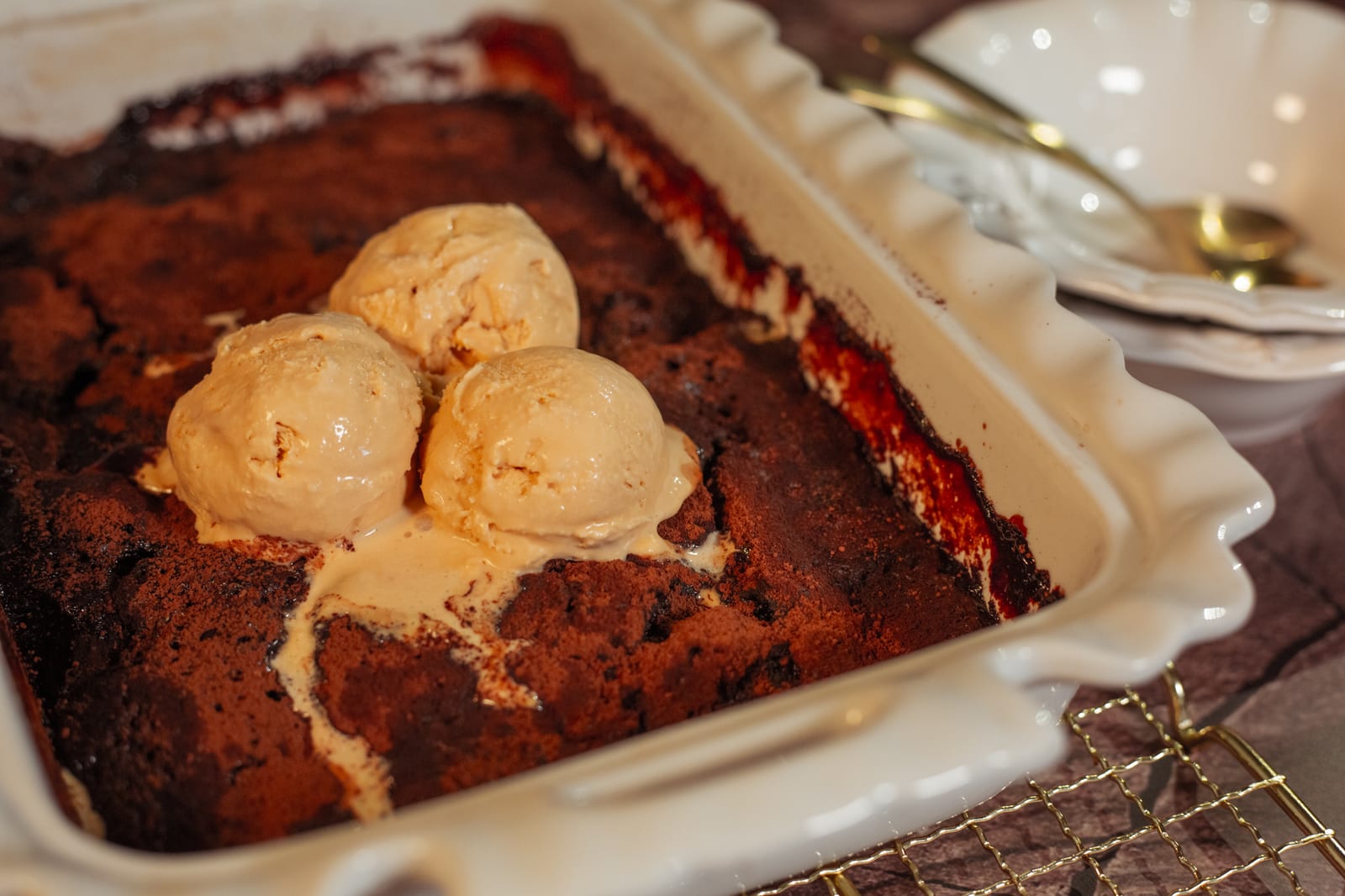 A chocolate self-saucing pudding topped with scoops of ice cream, in a white dish