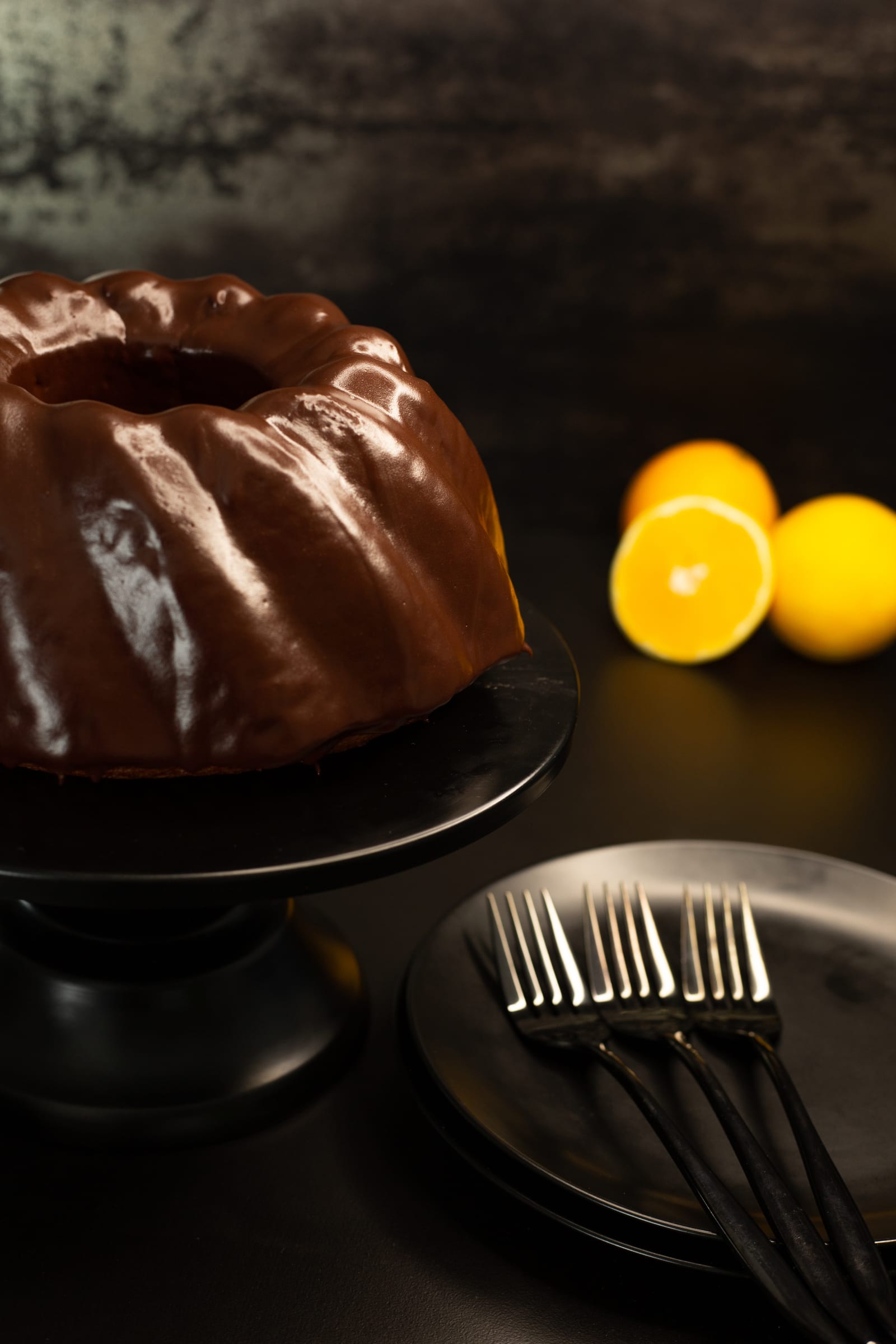 The chocolate-glazed bundt on its stand with plates and forks ready
