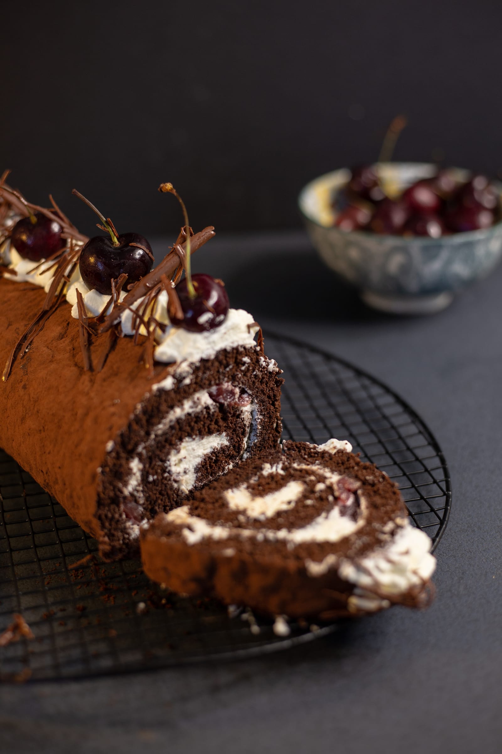 A cut Black Forest Swiss roll with slices fanned out, cherries behind